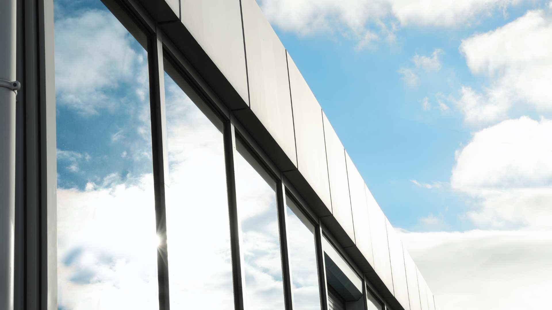 Modern glass building facade reflecting a blue sky with white clouds