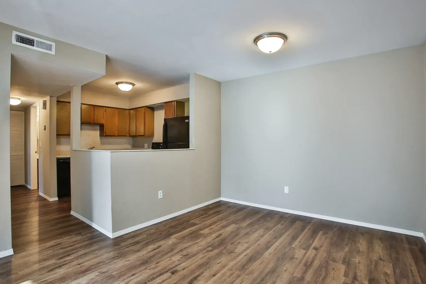 Photo of a wood-flooring living room with the kitchen and hallway in the background