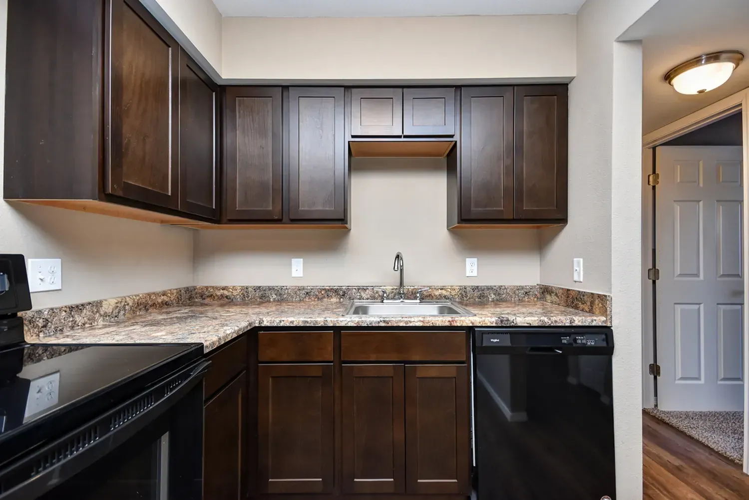 Photo of an L-shaped kitchen with an open door leading to a room in the background