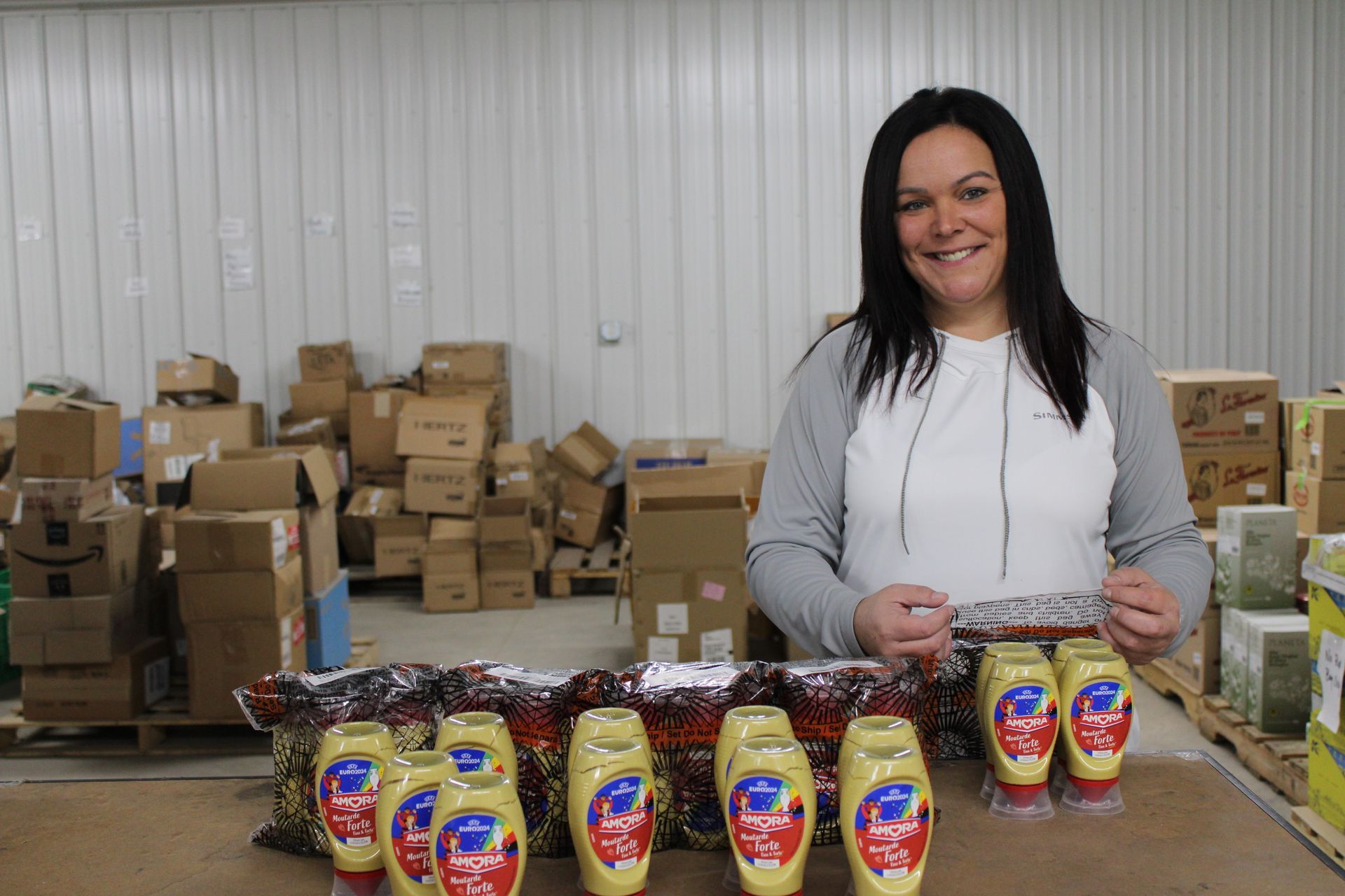 A woman is standing in front of a table filled with bottles of mustard.