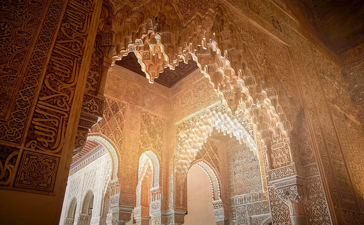 Ornate arches and walls with intricate carvings in a sunlit interior, possibly a historic palace.