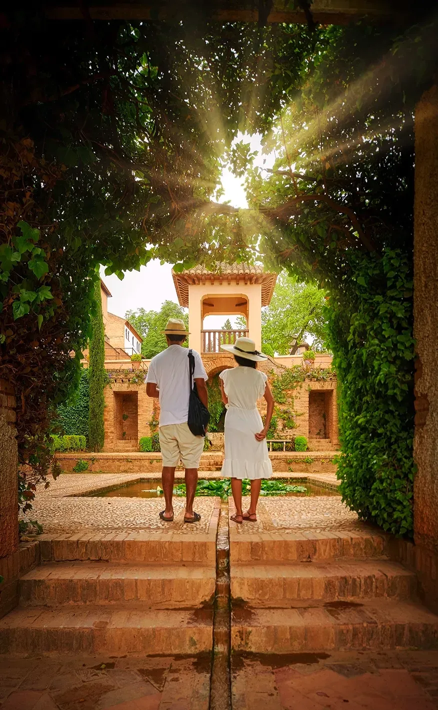 Couple admiring sunlit courtyard with archway and water feature.