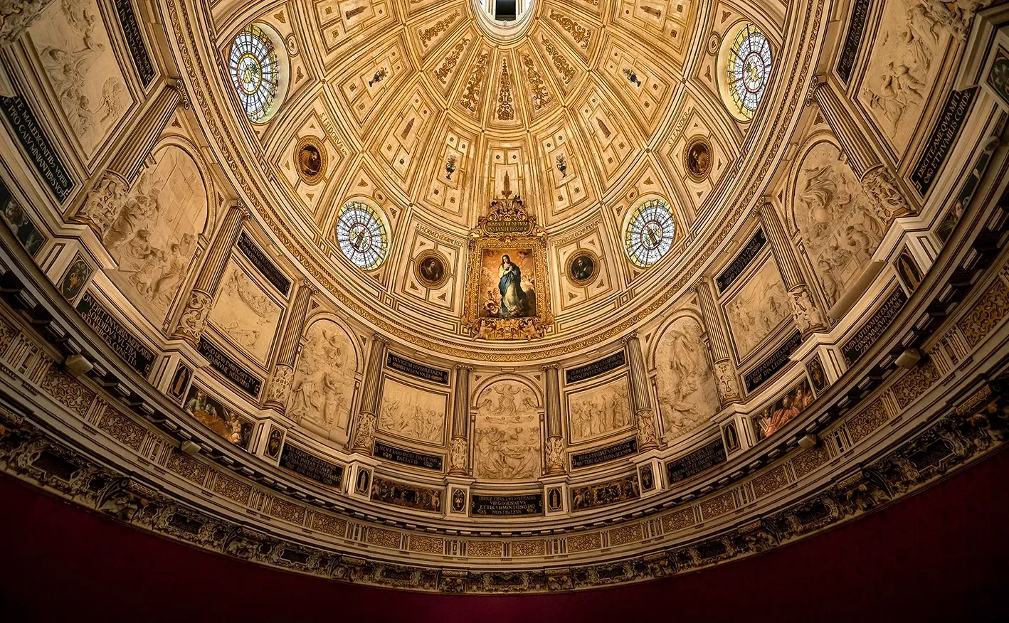 Ornate, gold-colored vaulted ceiling with intricate carvings, circular windows, and a central painting of a figure.