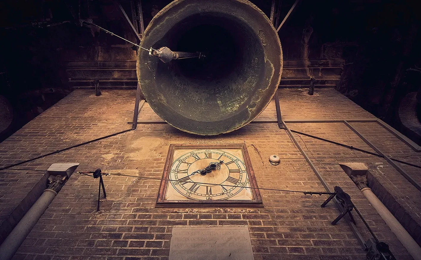 Large church bell above a clock, mounted on a brick tower.