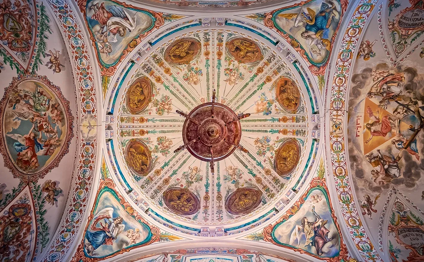 Ornate, painted ceiling of a dome with a central chandelier, featuring floral and figurative designs in pastel colors.