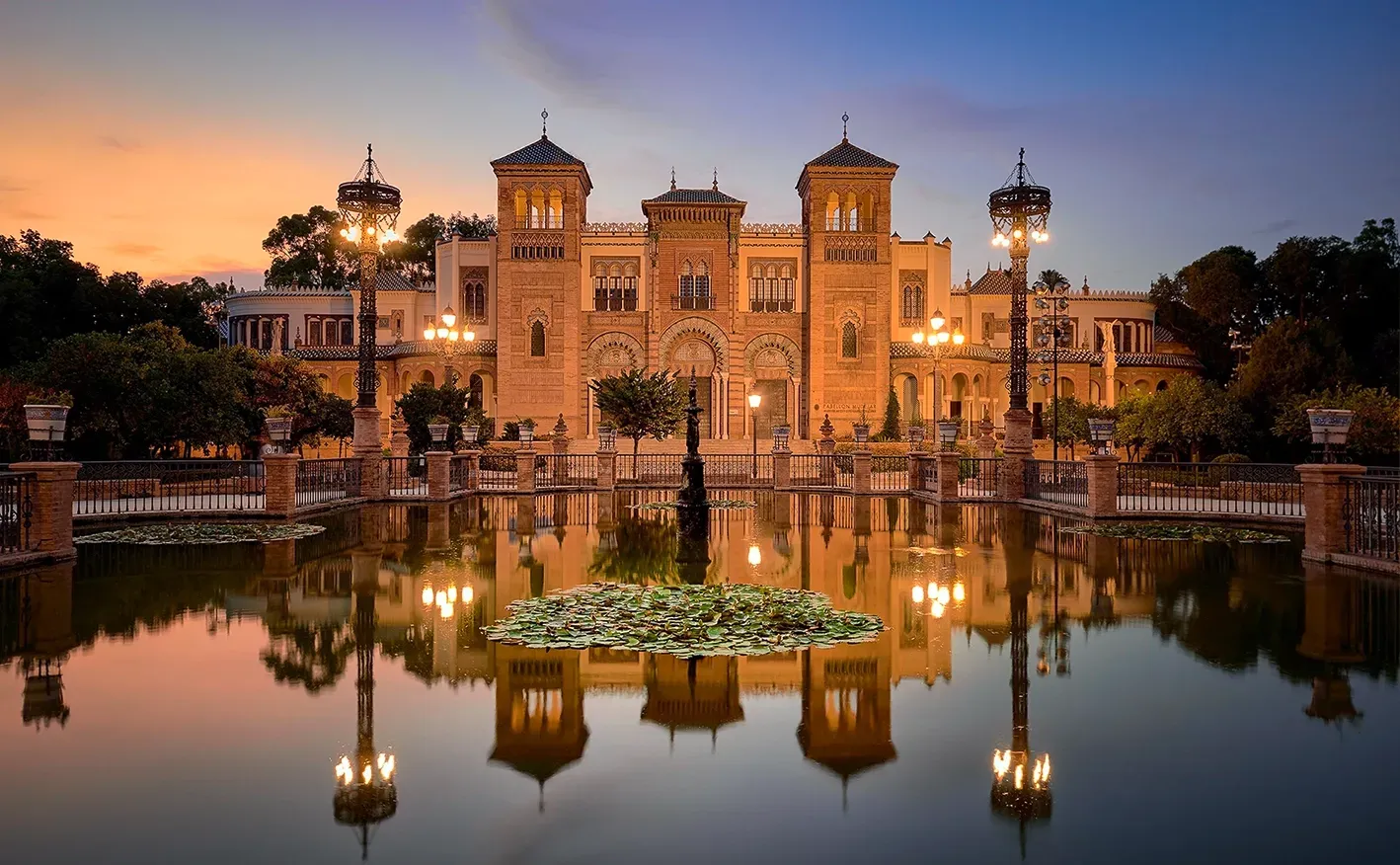 Palace reflected in calm water at dusk; warm lighting, ornate architecture.