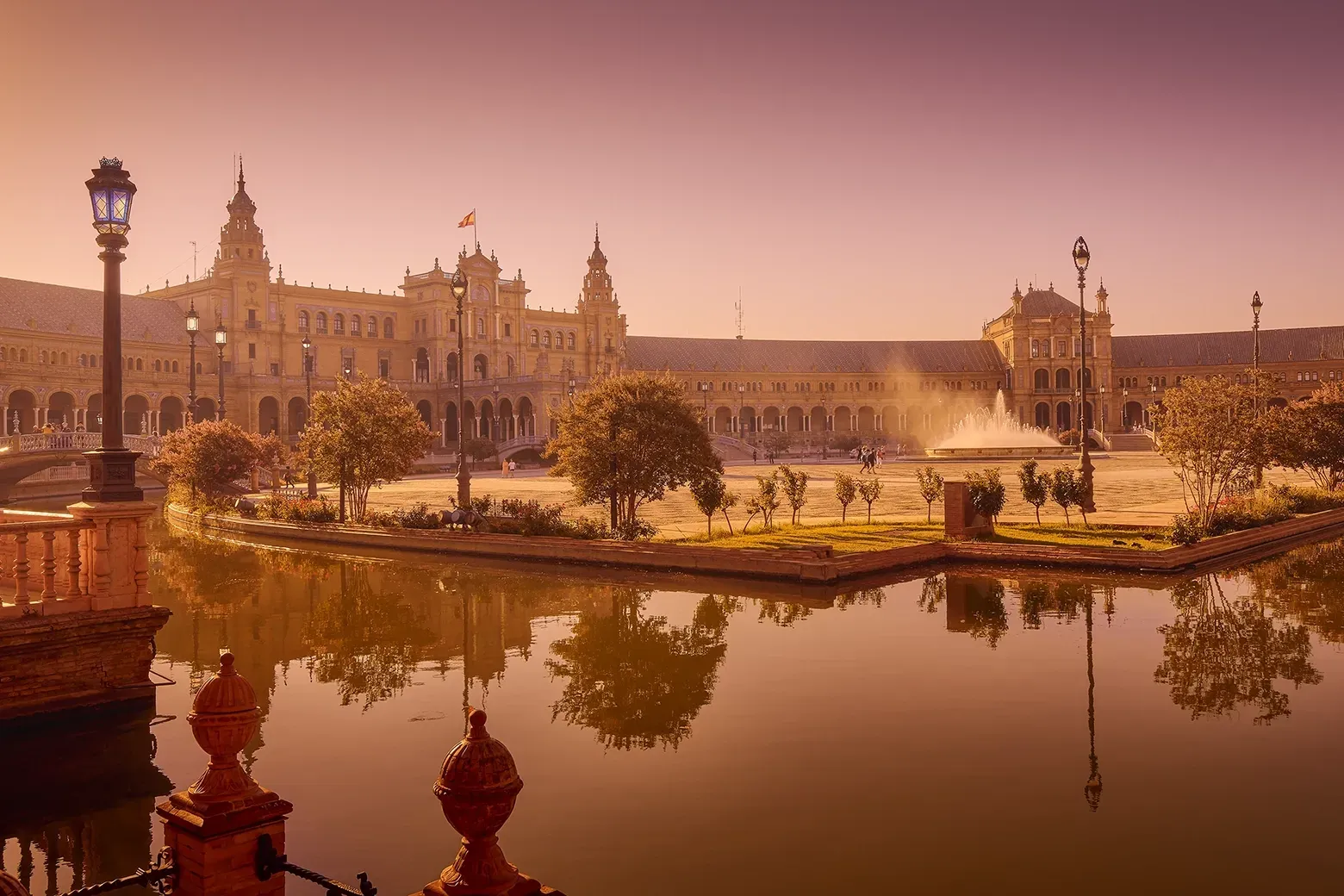 Plaza de España in Seville, Spain. Elegant architecture reflected in a serene canal under a warm, dusky sky.