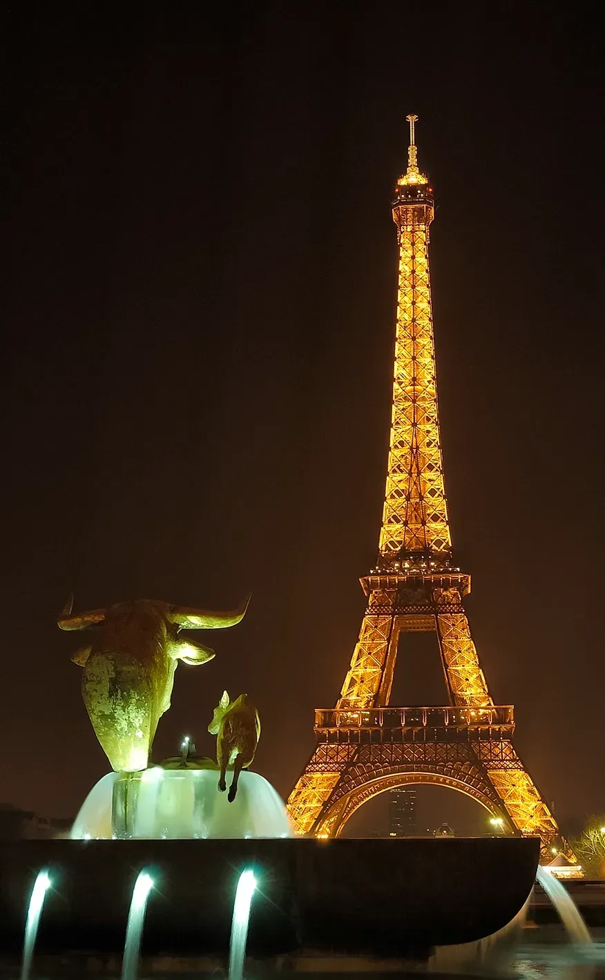 Eiffel Tower illuminated at night, with a fountain featuring golden sculptures in the foreground.