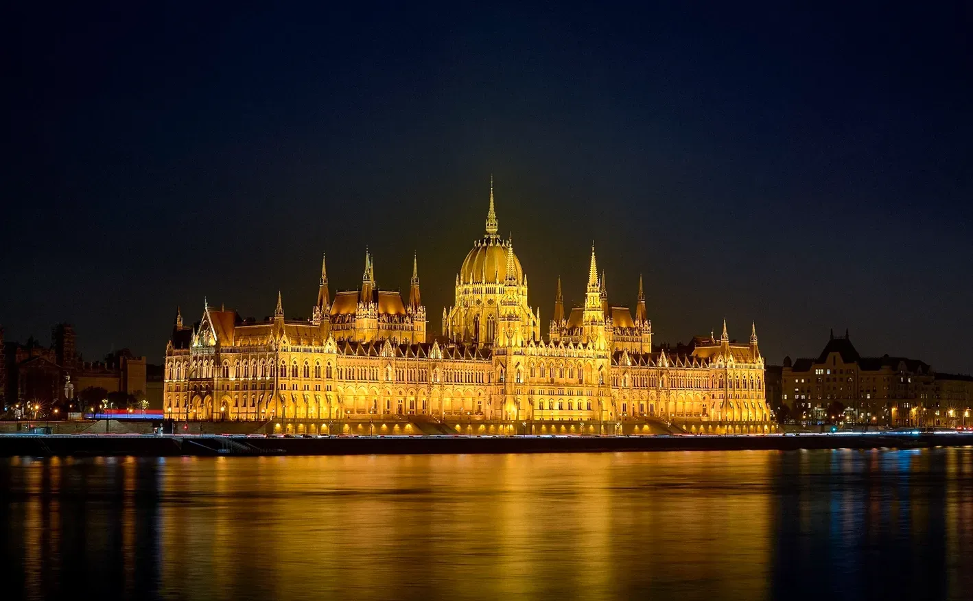 Hungarian Parliament Building illuminated at night, reflected on water.