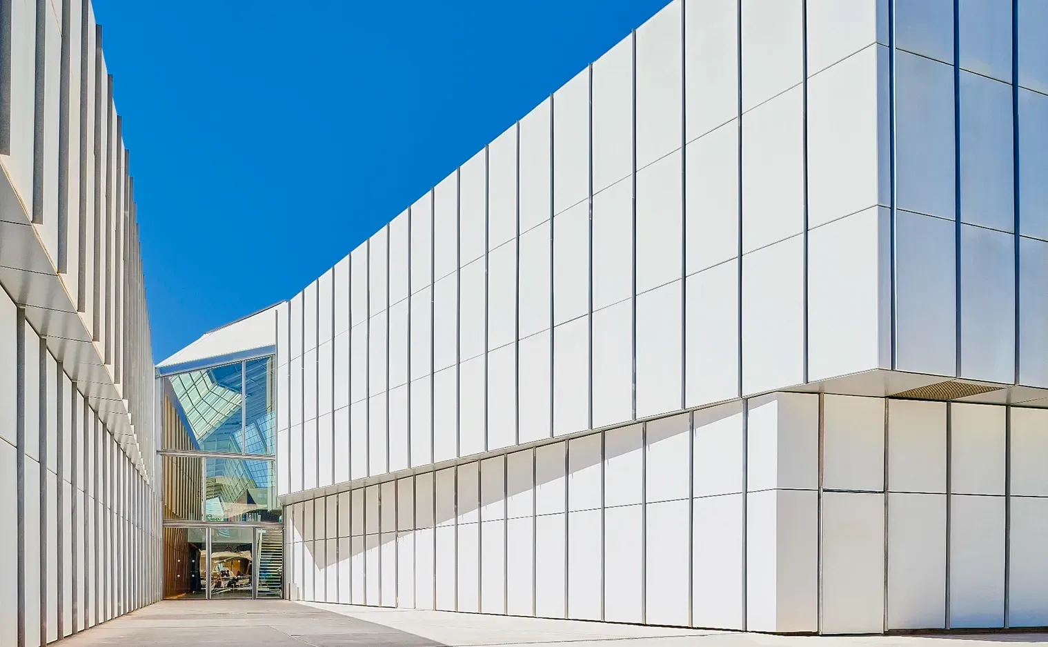 White, modern building with a series of vertical panels, blue sky in background.
