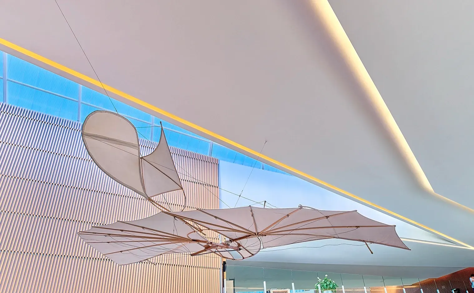 An art installation: stylized, open-winged model aircraft hanging from a white ceiling, in a modern building.