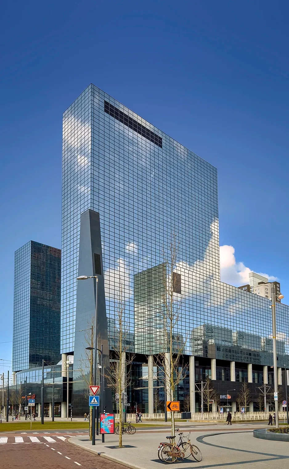Glass skyscraper reflecting the sky, other buildings in the background, bikes in front.