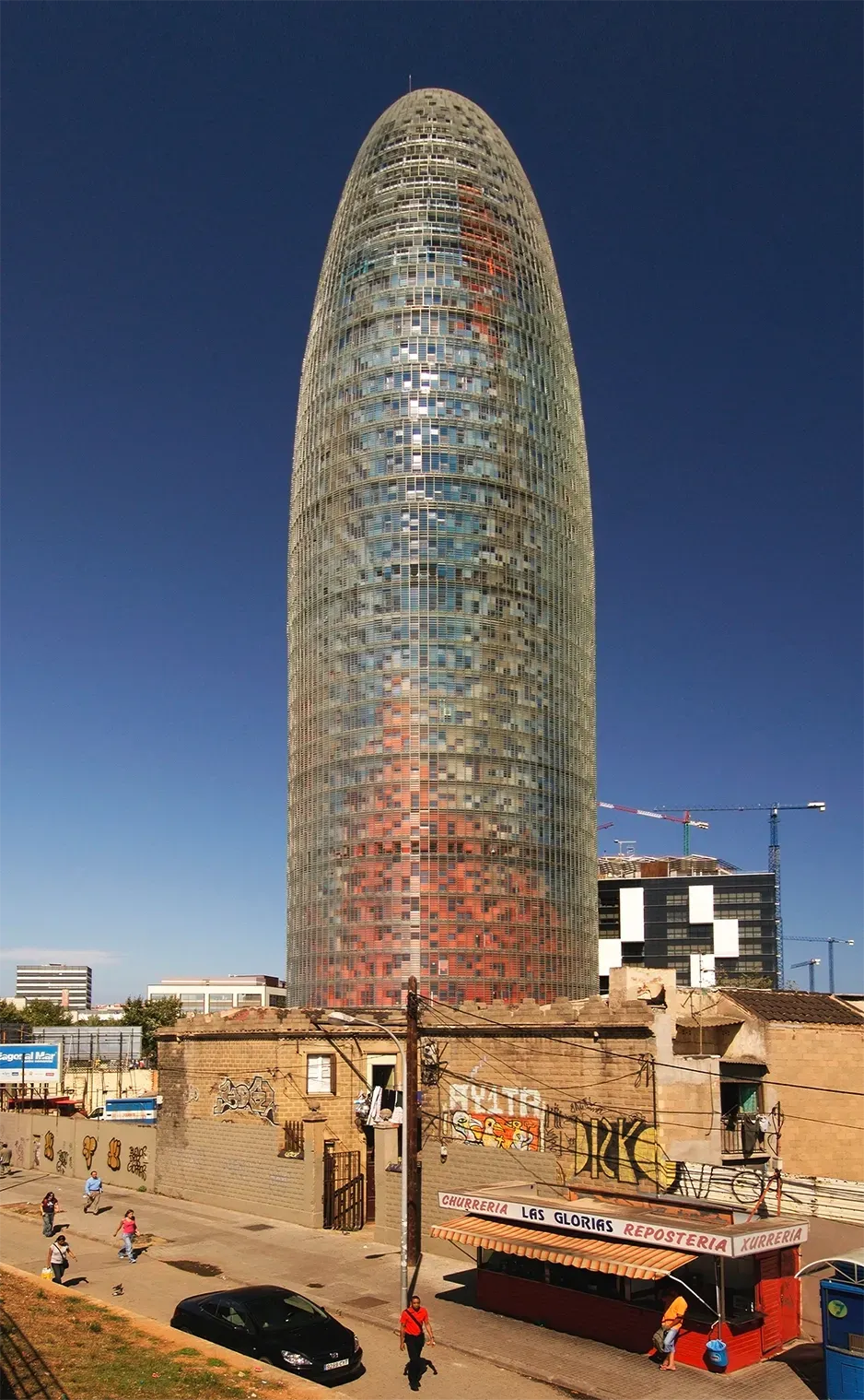 Agbar Tower, a tall glass skyscraper, with red and blue sections, against a clear blue sky in Barcelona.