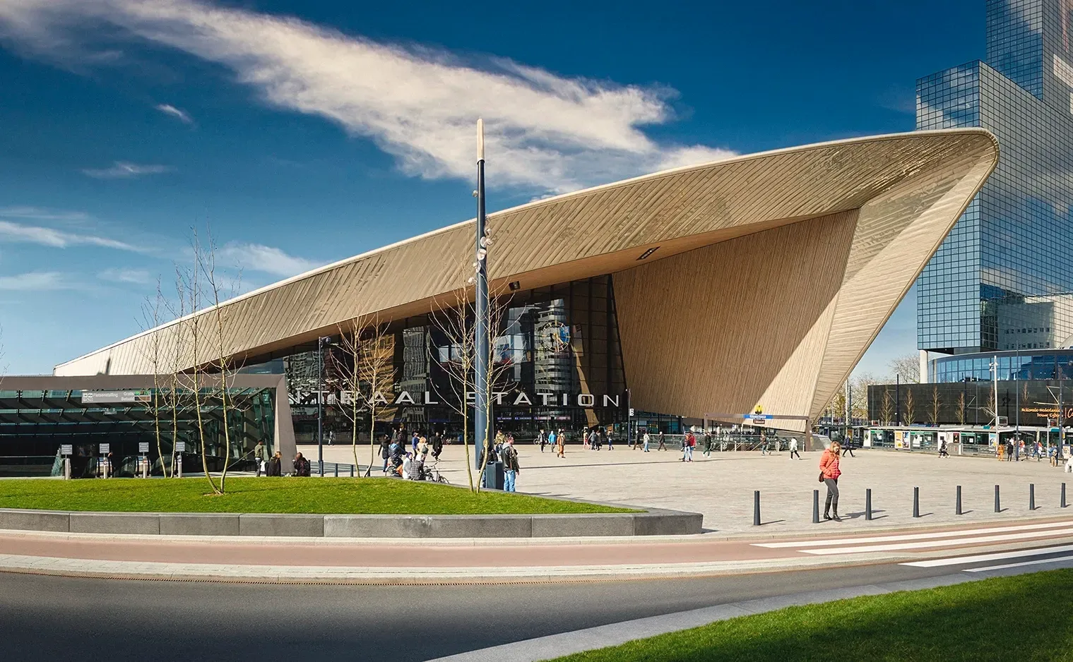 Modern train station with a slanted, brown roof; people outside on a sunny day.