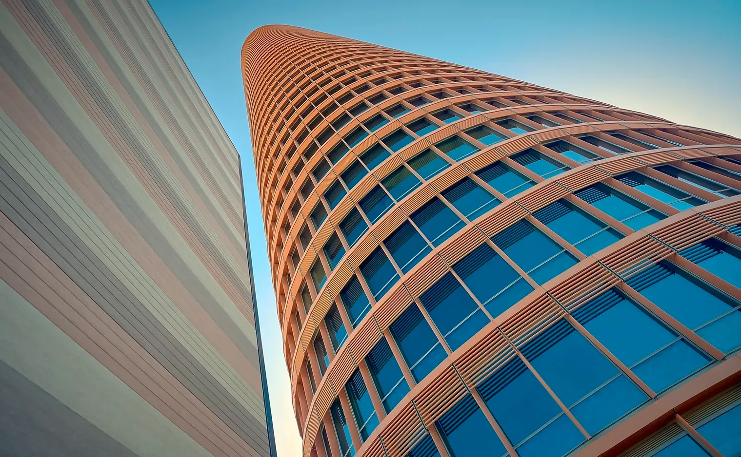 Tall, cylindrical brick building with blue glass windows, viewed from below with clear blue sky.