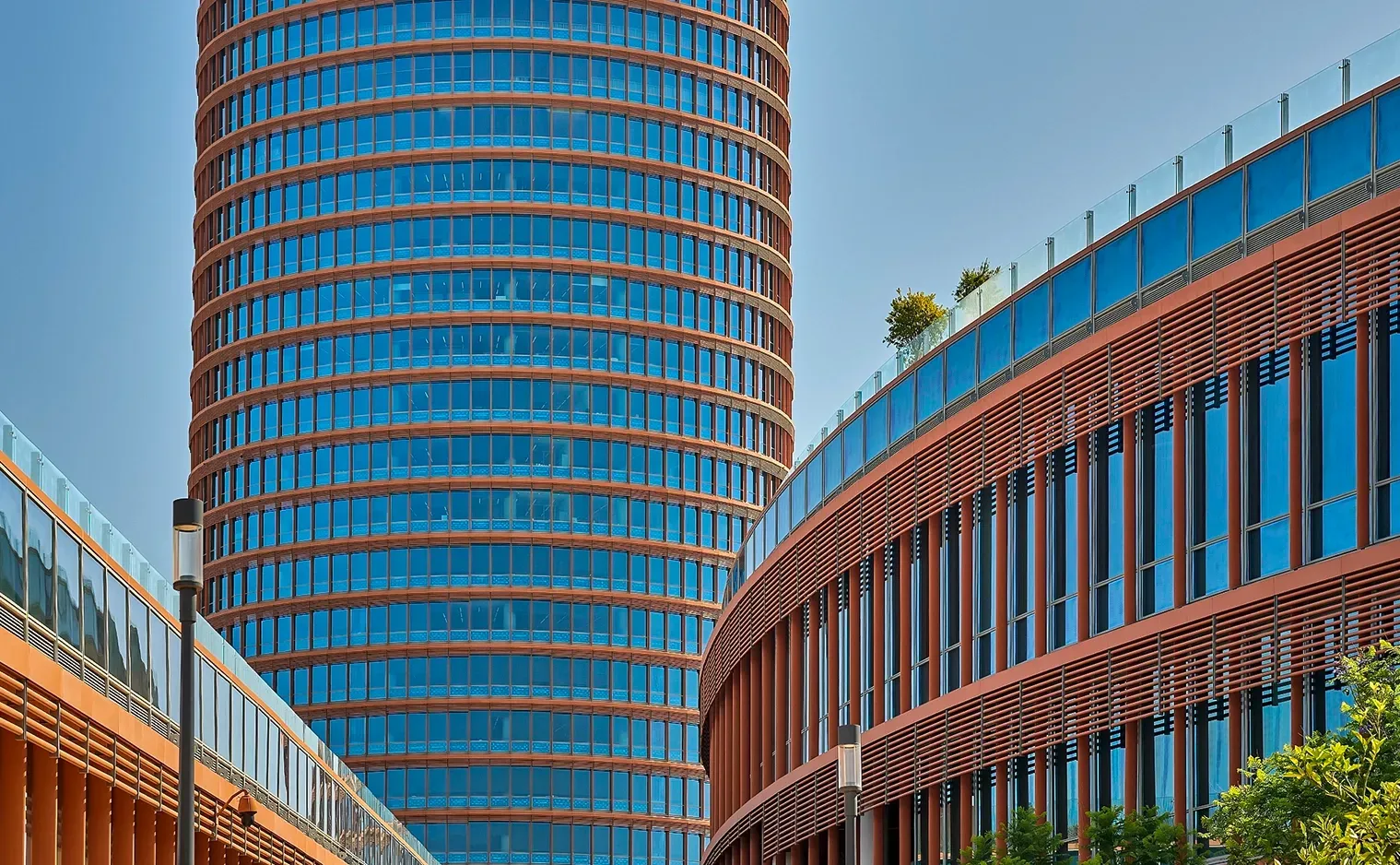 Modern cylindrical skyscraper and curved buildings with blue glass windows and terracotta-colored facades.