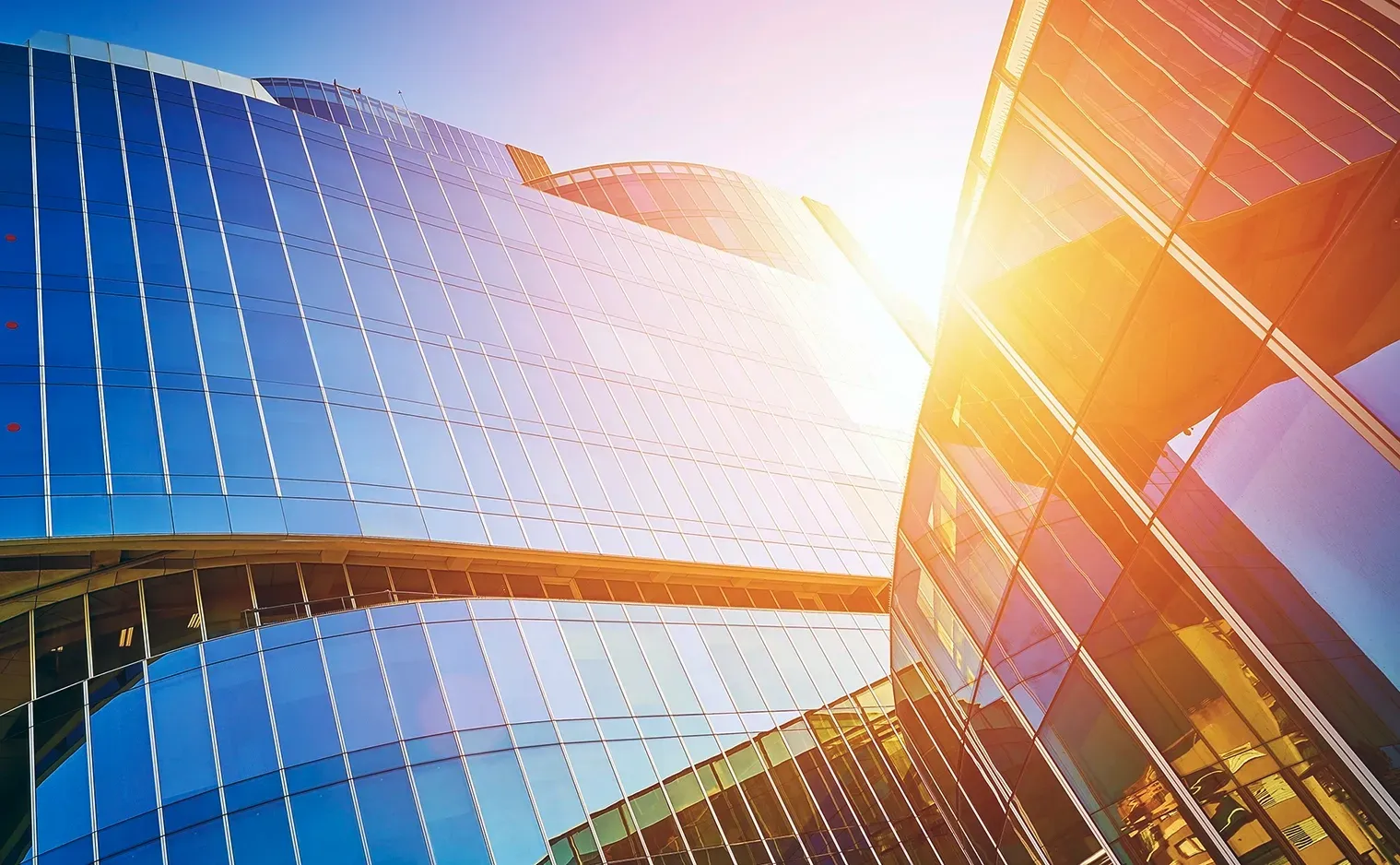 Glass skyscrapers, reflecting blue sky and bright sunlight.