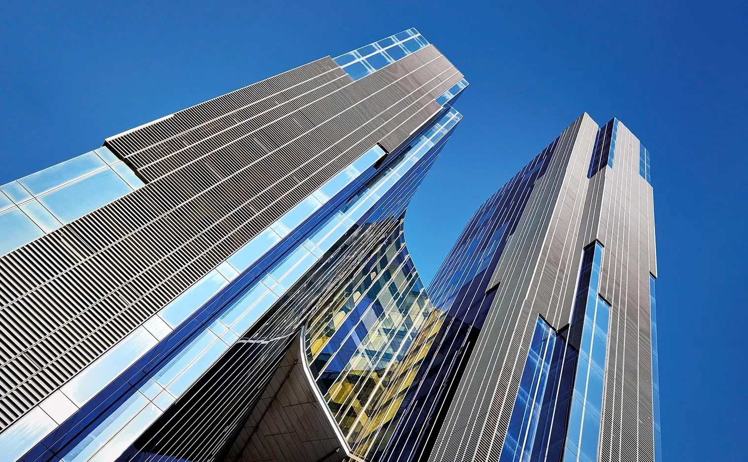 Skyscrapers with reflective glass and metal facade against a bright blue sky.