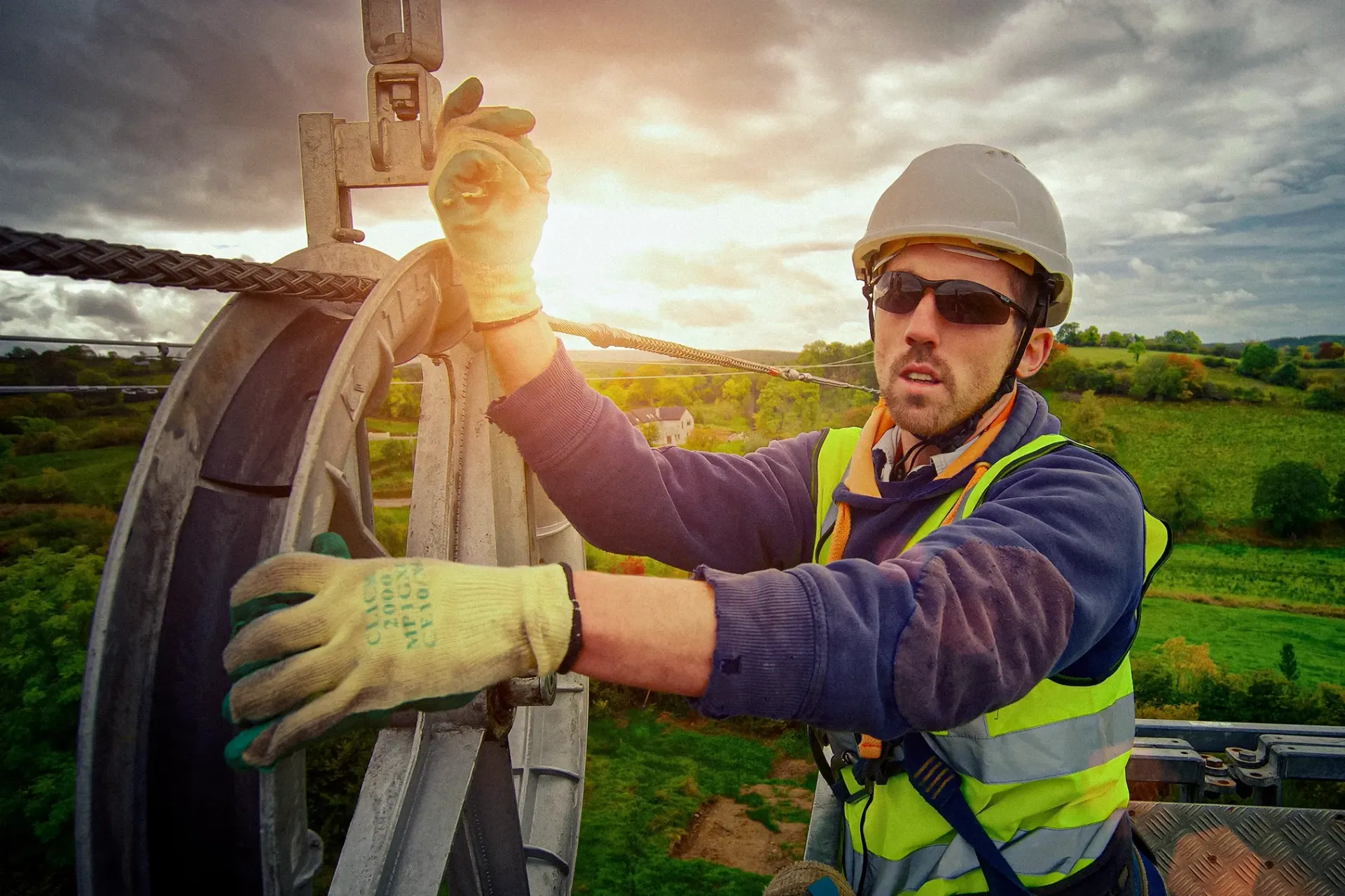 Construction worker in safety gear, adjusting equipment outdoors, bright sunlight.