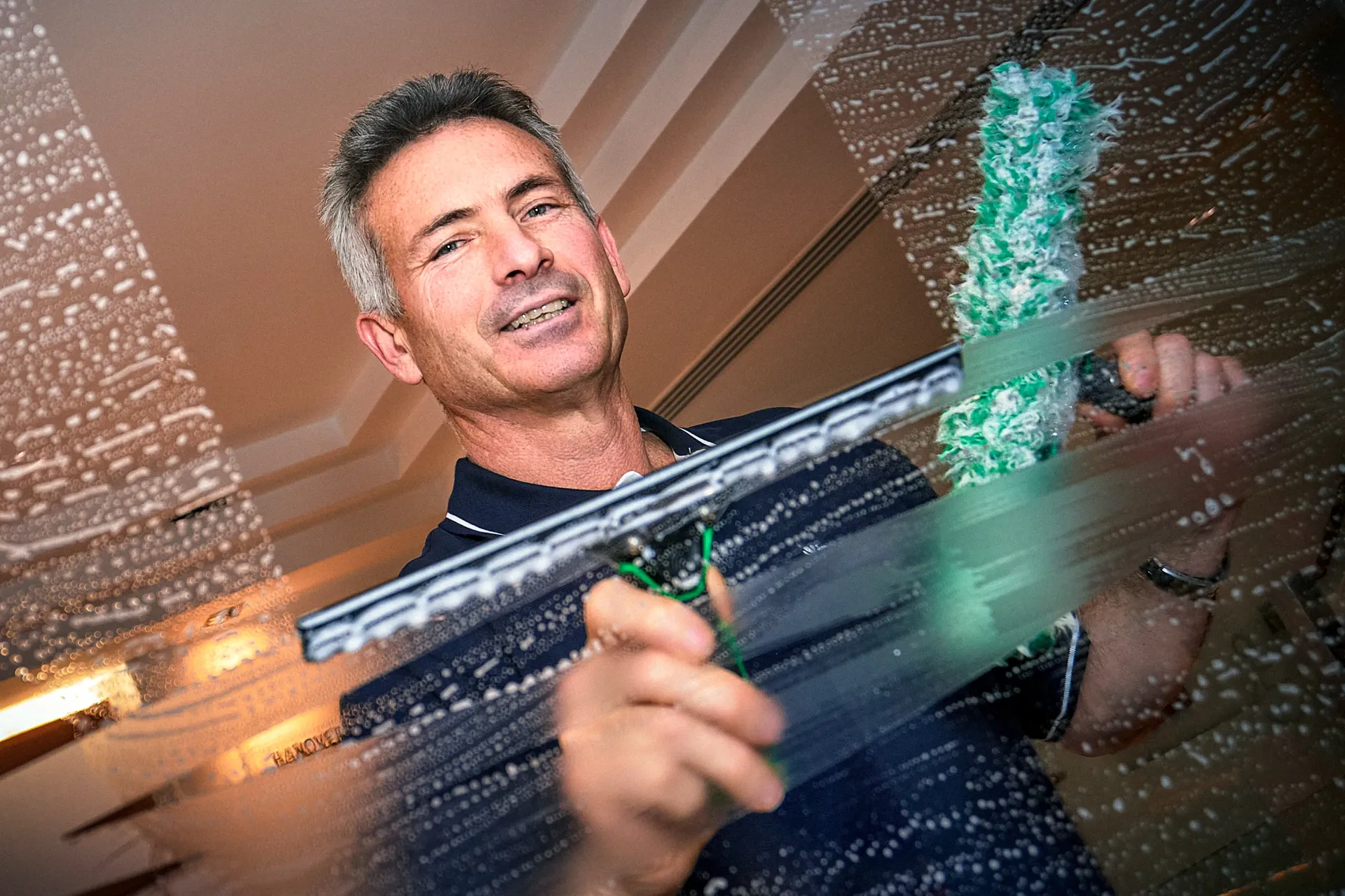 Man squeegeeing a soapy window, smiling, indoors.