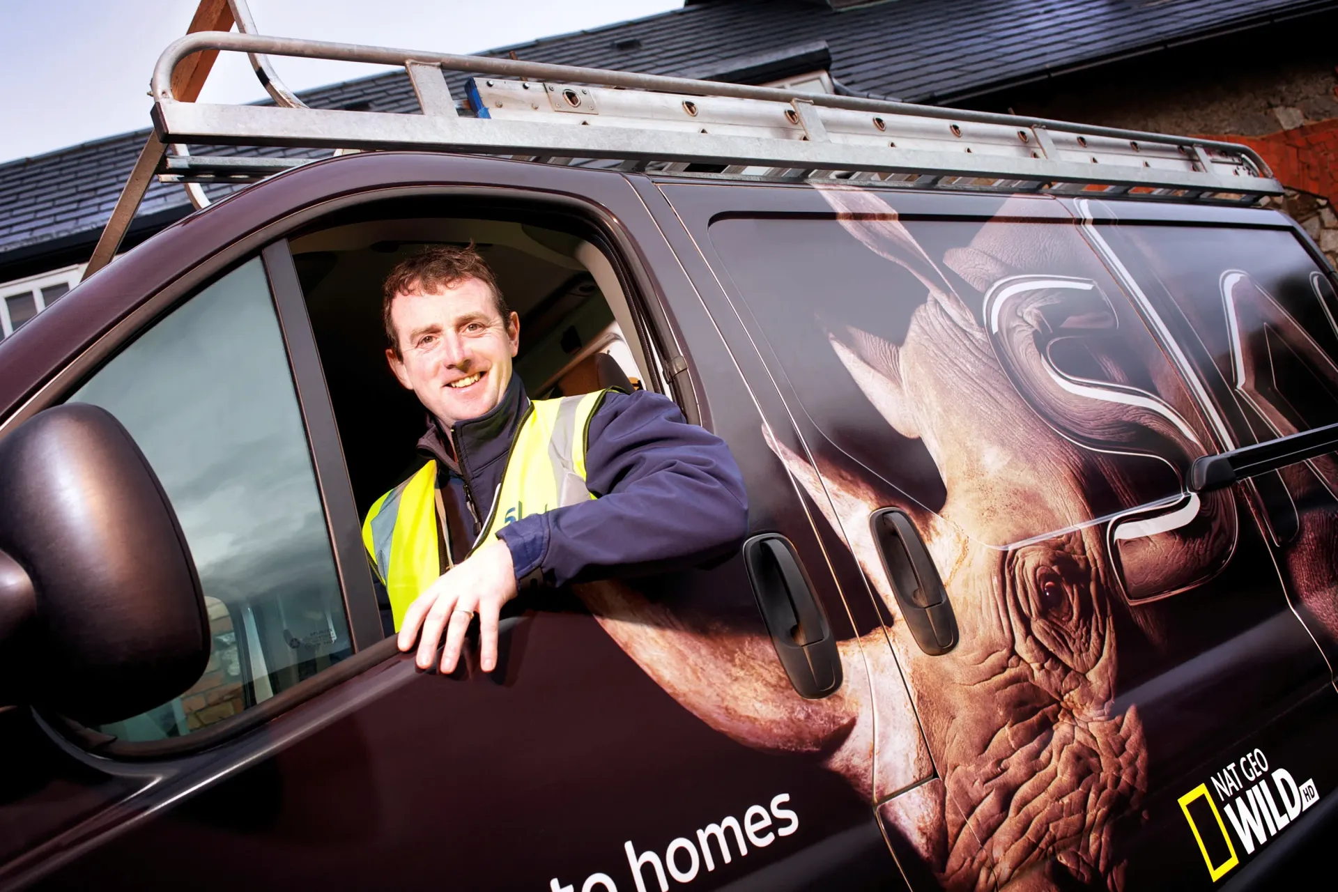 Man in safety vest smiles from van window, featuring National Geographic Wild logo and deer graphic.
