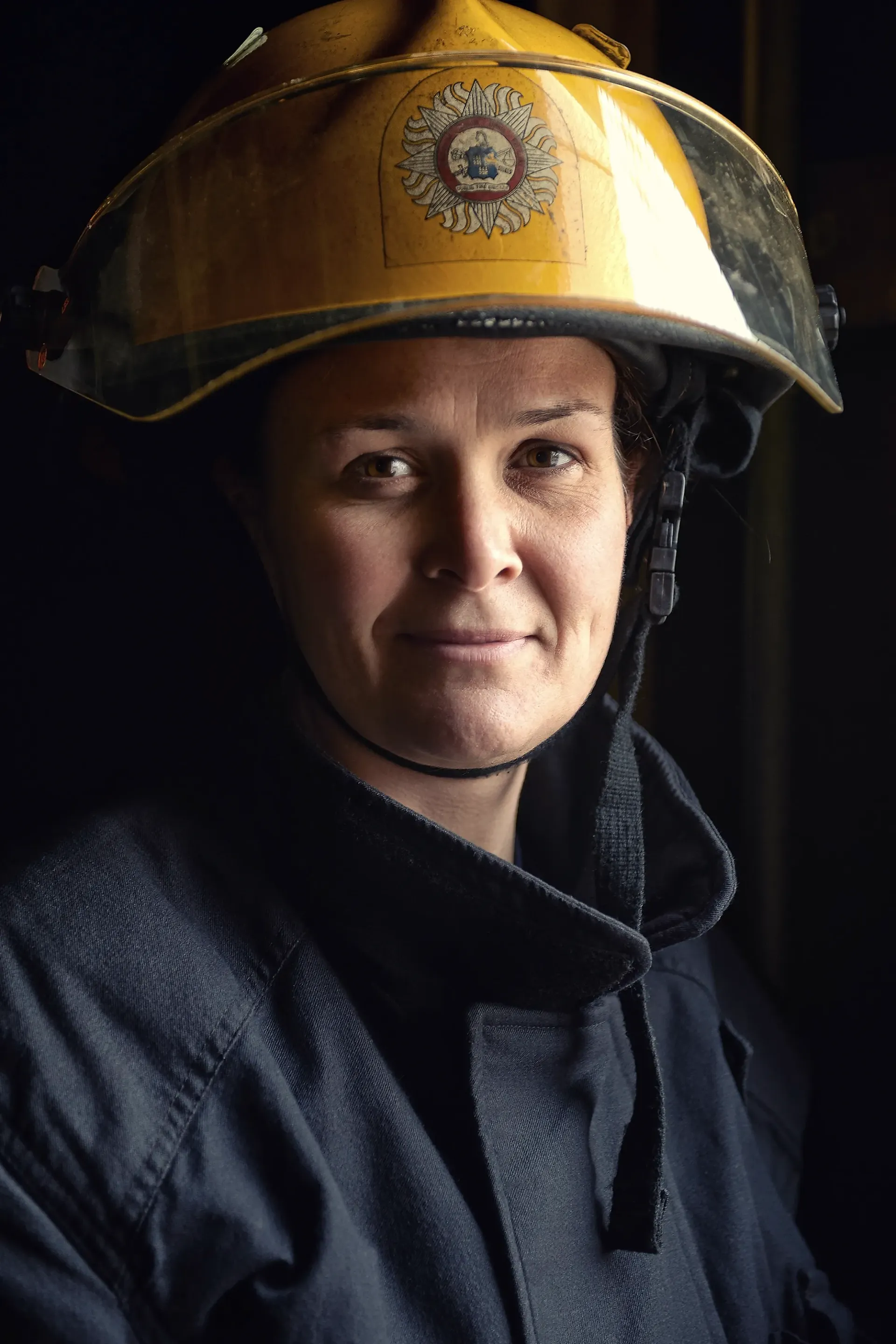 Firefighter in a yellow helmet and navy uniform, looking toward the camera.