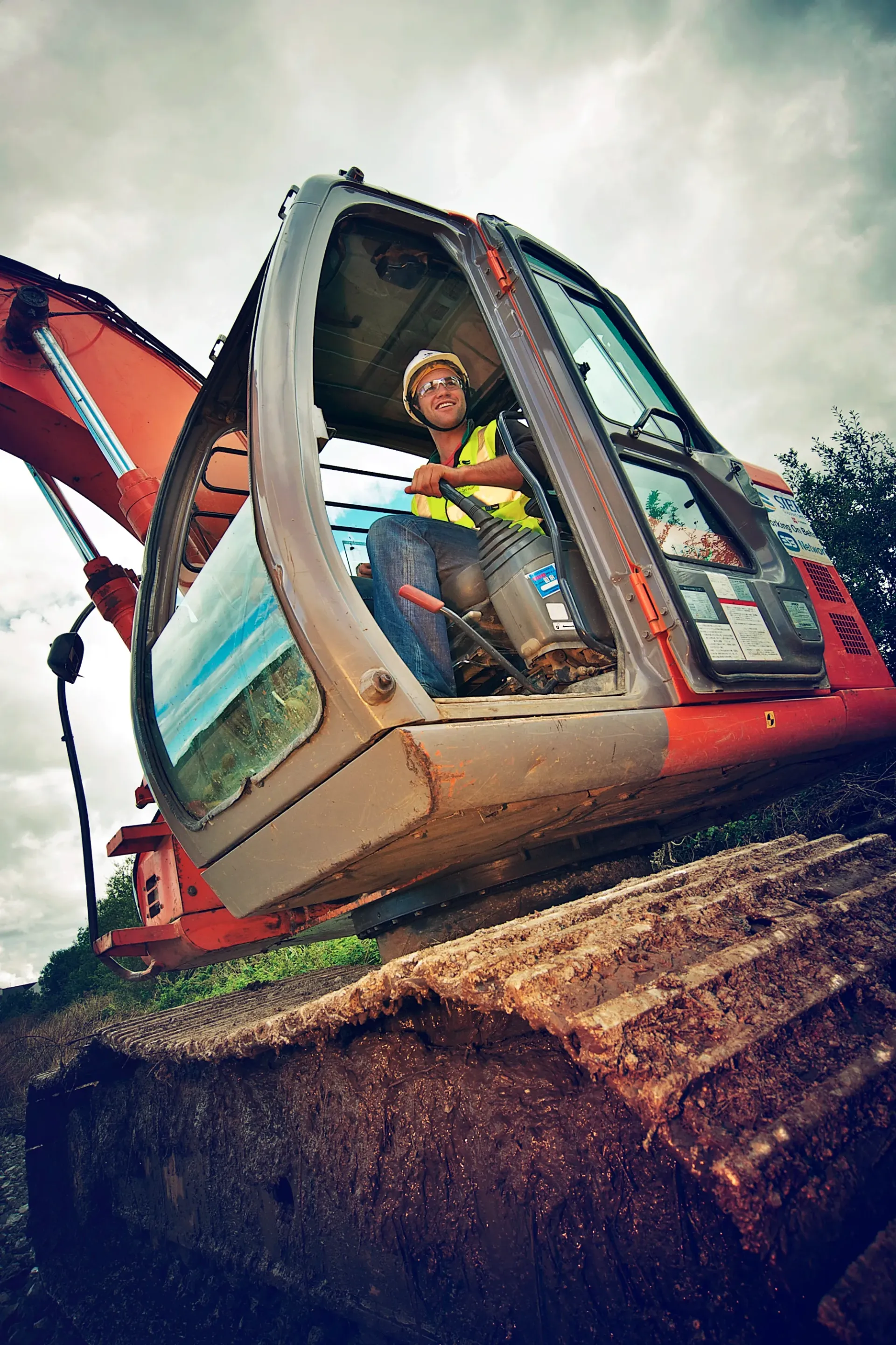 Construction worker in excavator cab, wearing safety vest and hard hat.