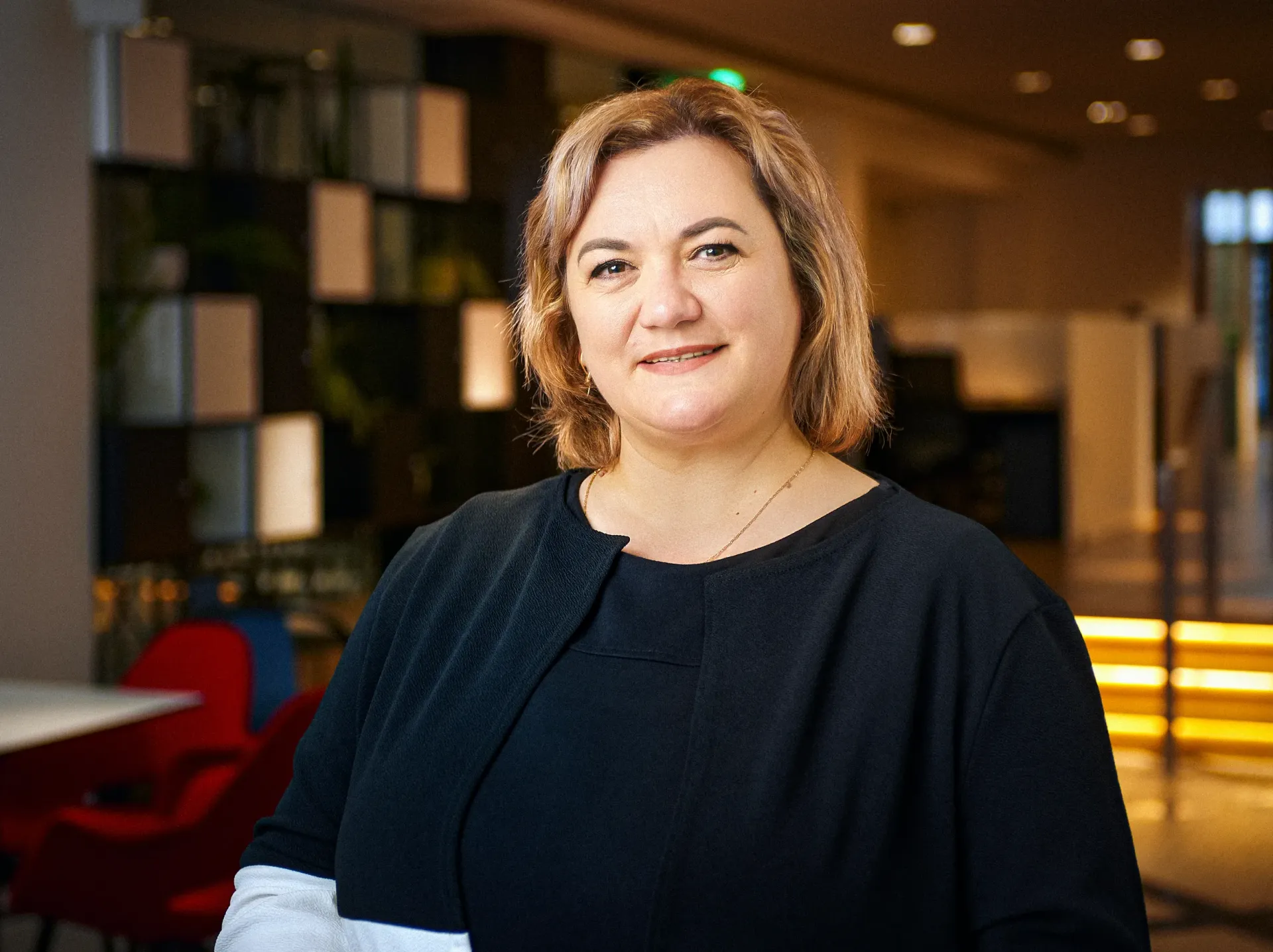 Woman in black top smiles, standing in a modern office.