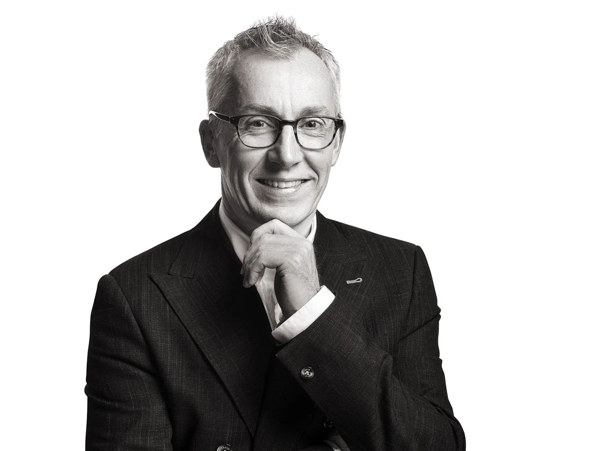 Man with glasses, hand on chin, smiling, wearing a suit jacket and dress shirt.