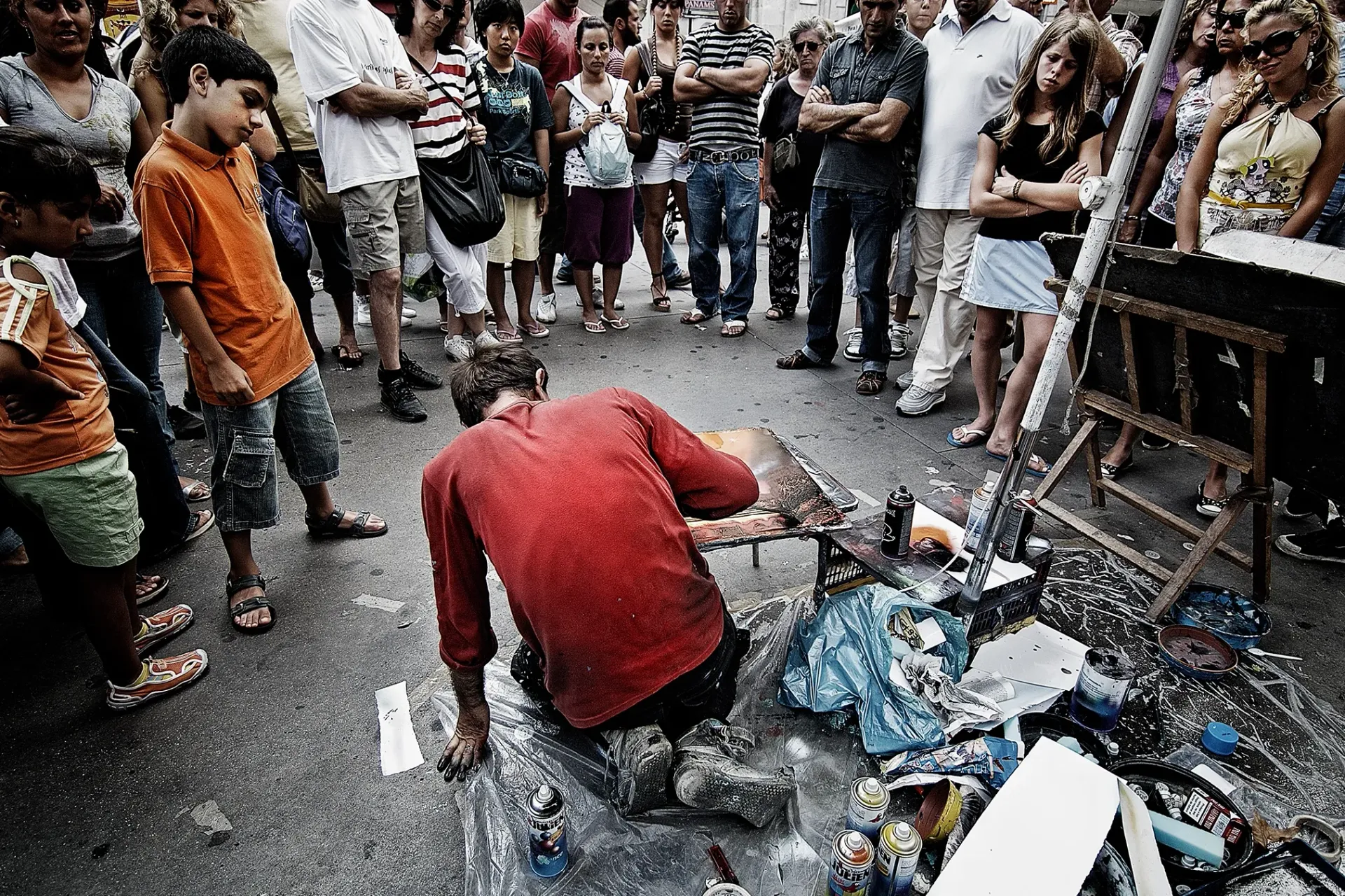 Artist on street surrounded by onlookers; he is working on a piece on the ground.