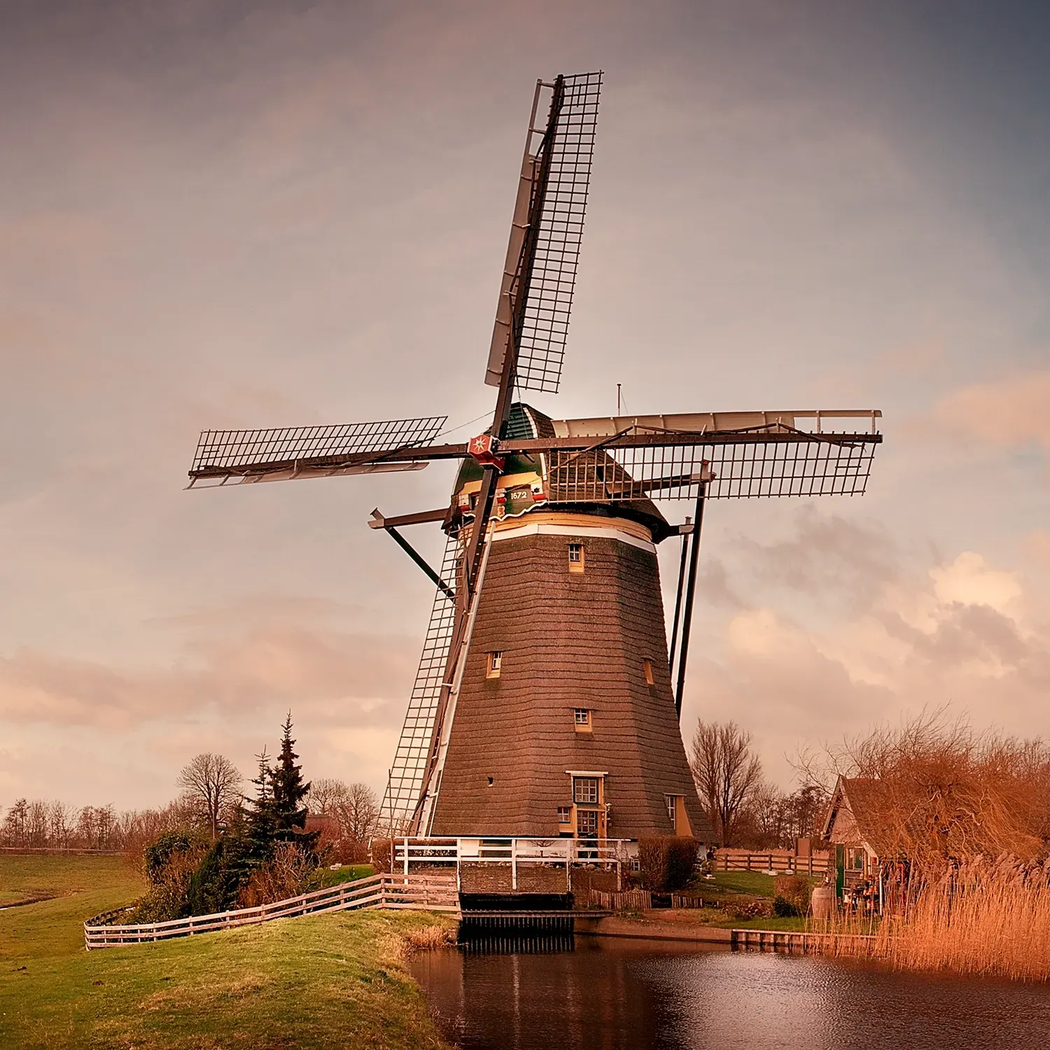 Windmill on a canal in the Netherlands, with blades outstretched against a dusky sky.