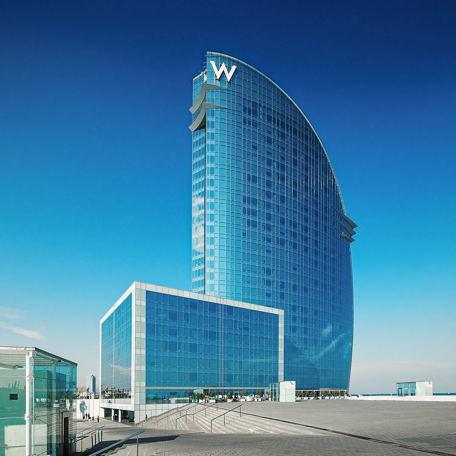 W Hotel Barcelona, a tall, glass-faced building against a bright blue sky.