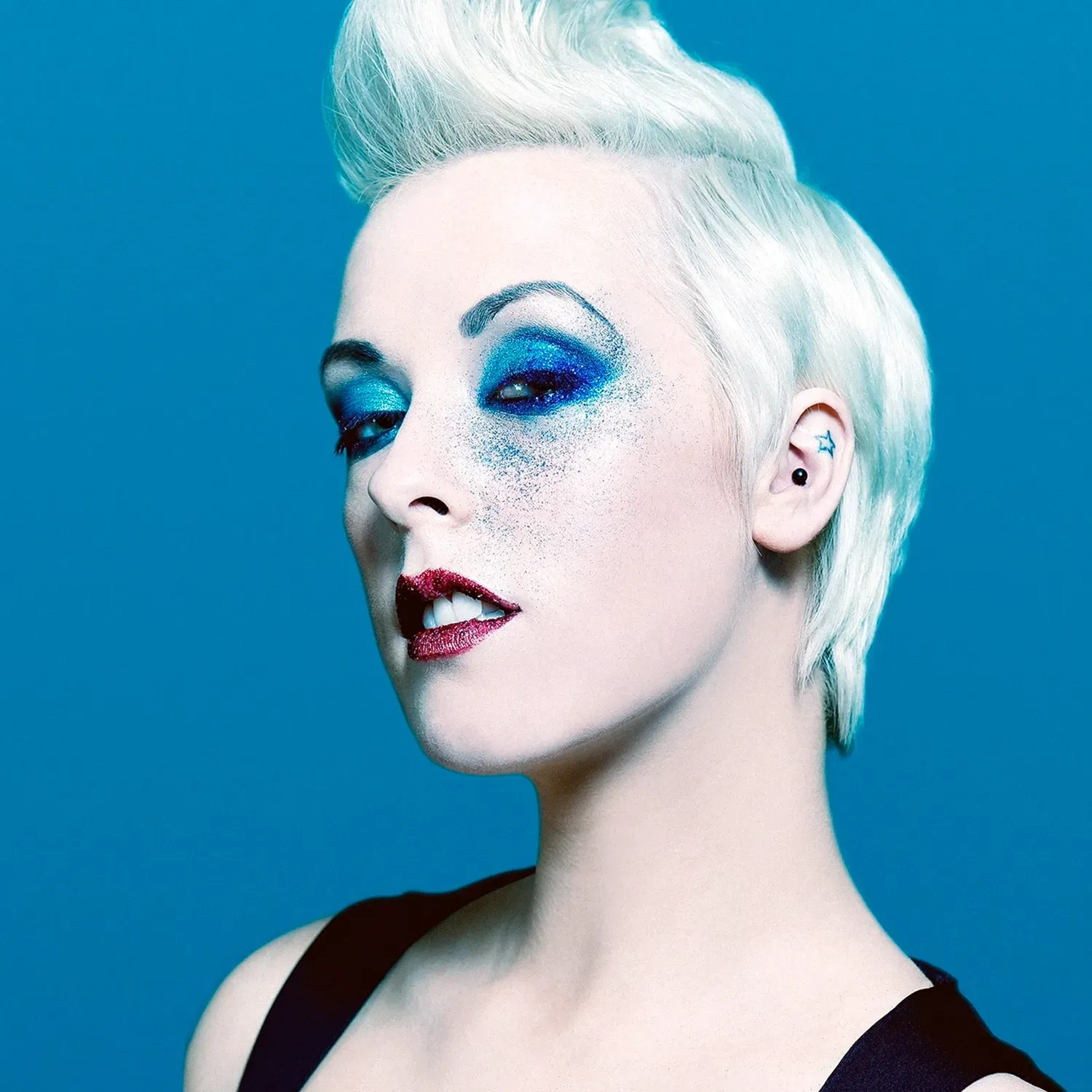 Woman with white, sculpted hair and blue eyeshadow against a blue background.