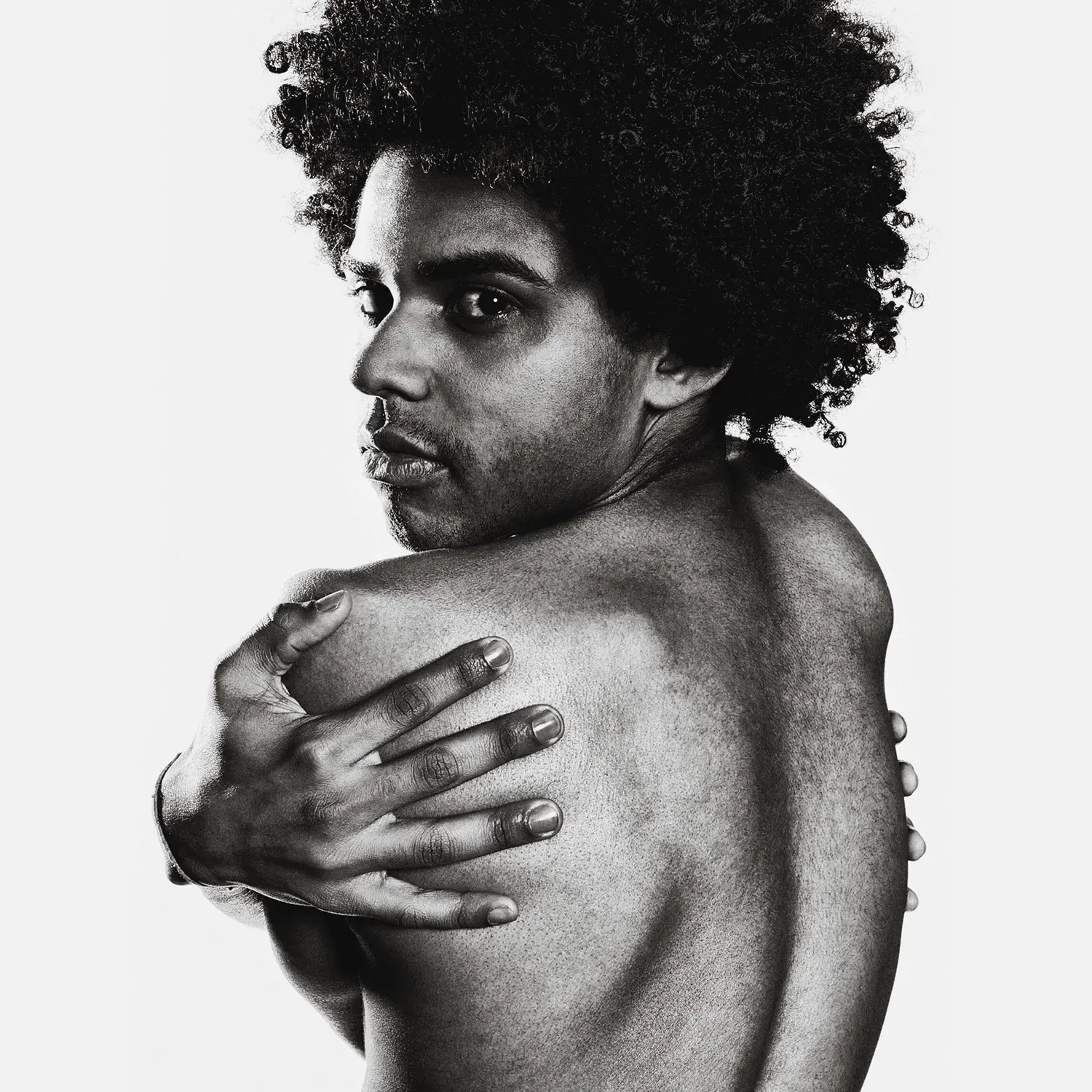 Man with afro, looking over his shoulder, embracing himself, black and white.