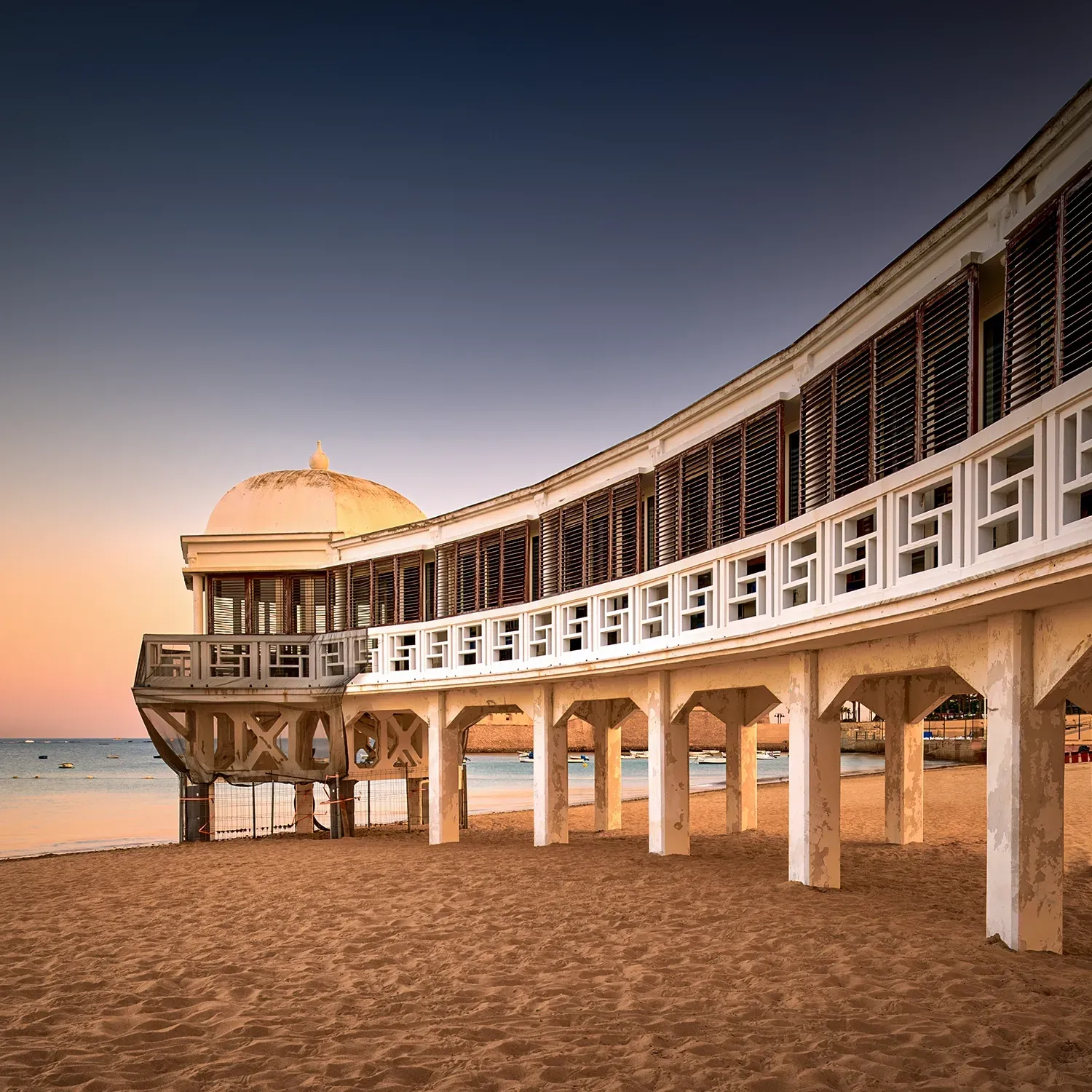 Beachfront building with arched facade and open porch on a sandy beach.
