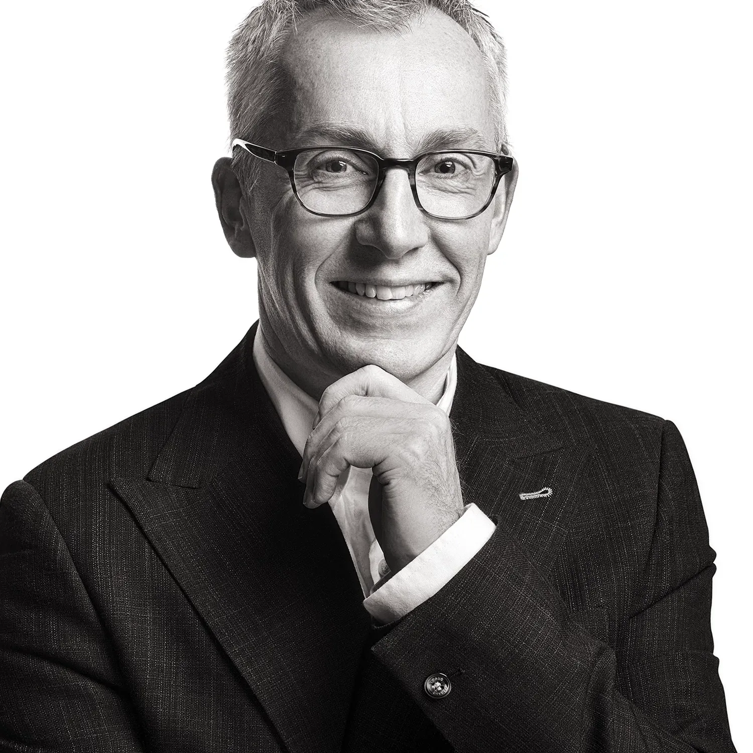 Man in suit and glasses smiling, hand on chin. Black and white photo.