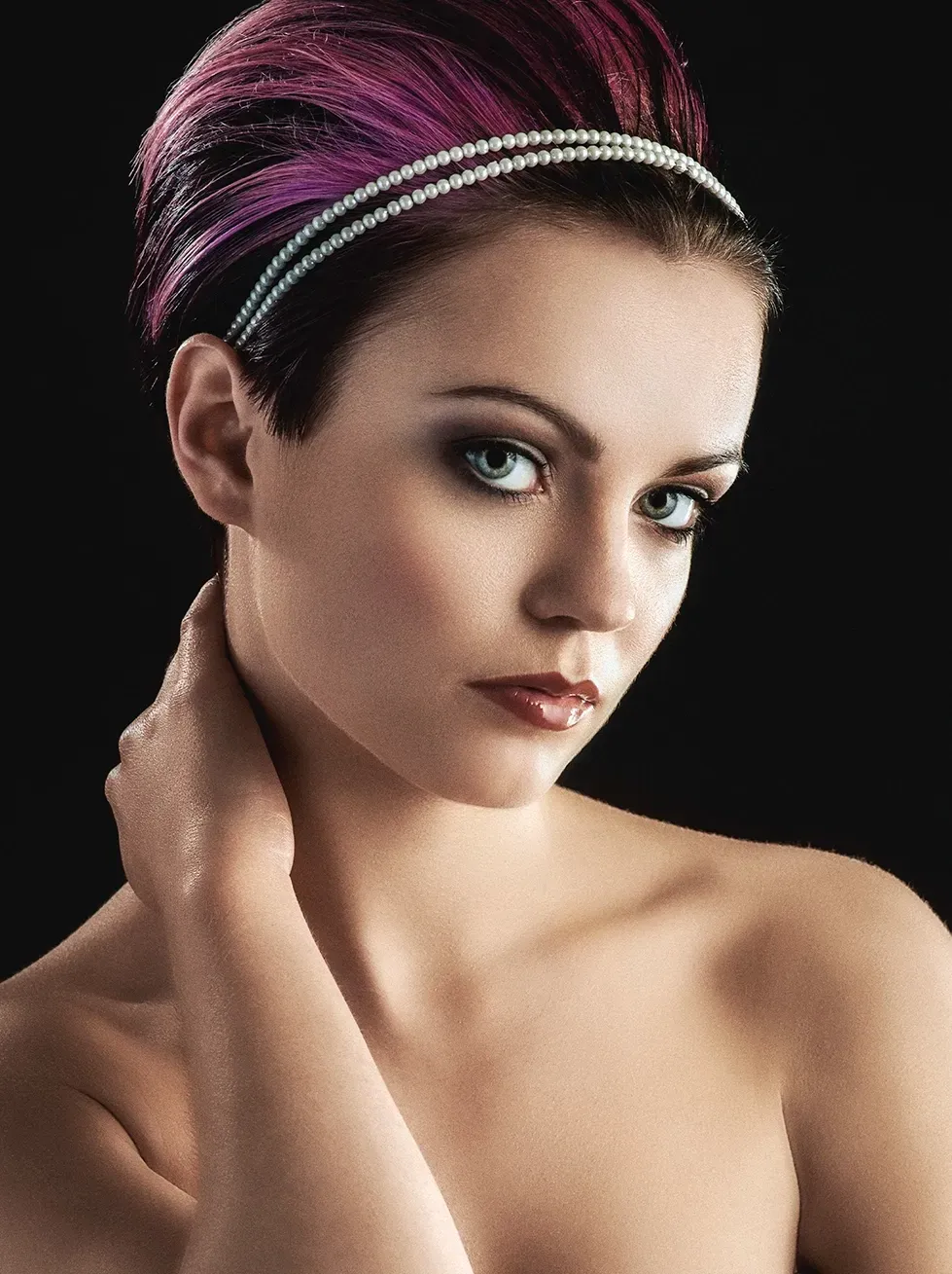 Woman with short, purple-streaked hair wearing a jeweled headband, dark eye makeup, and gazing at the viewer.