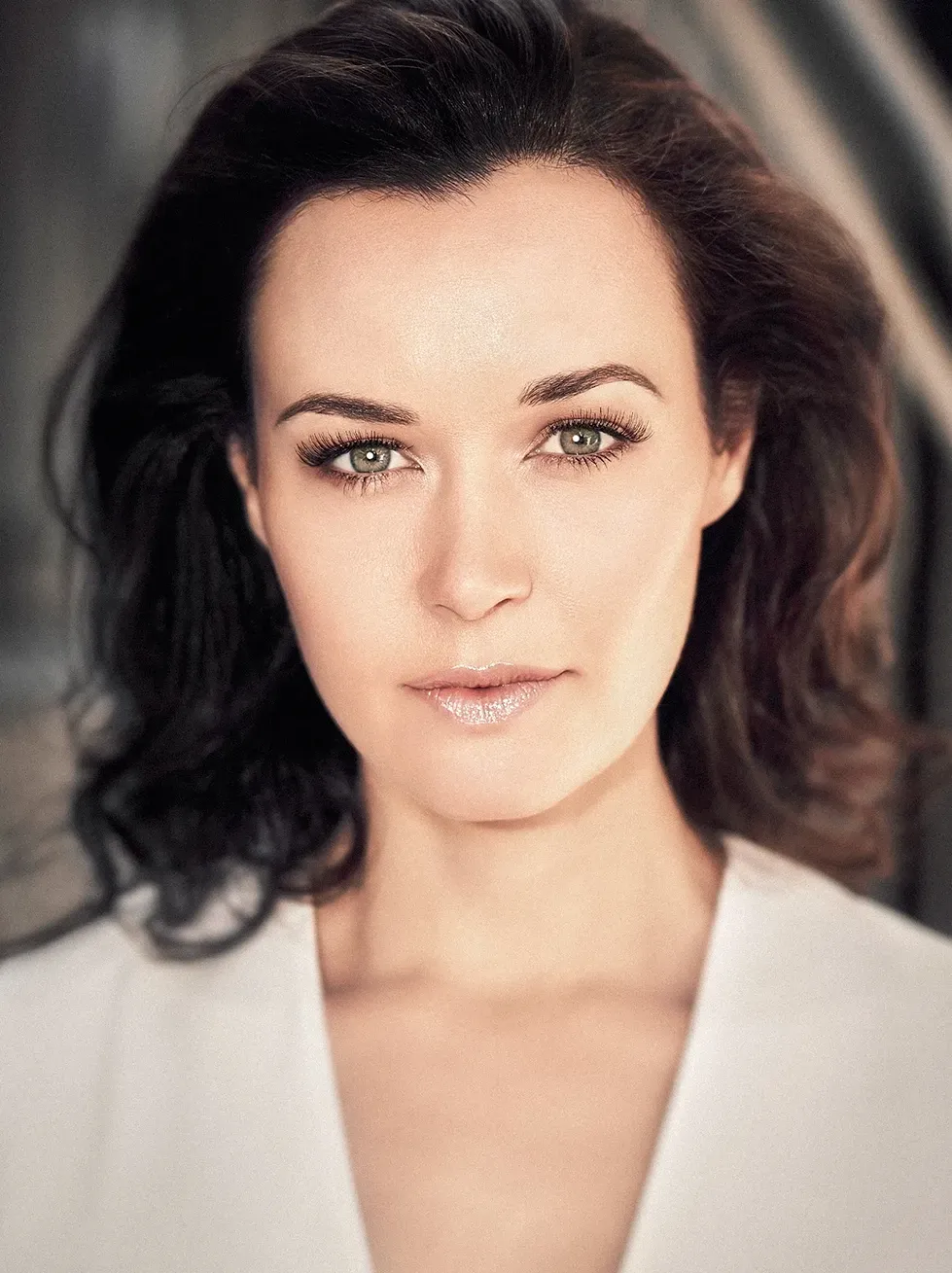Woman with brown hair and green eyes, wearing a white top, looking directly at the camera.