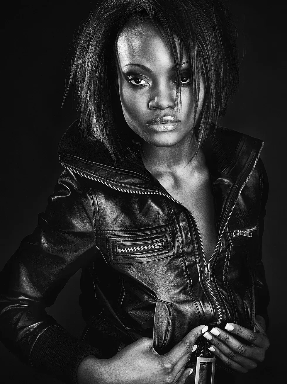 Woman wearing a black leather jacket, looking towards the camera with a serious expression.