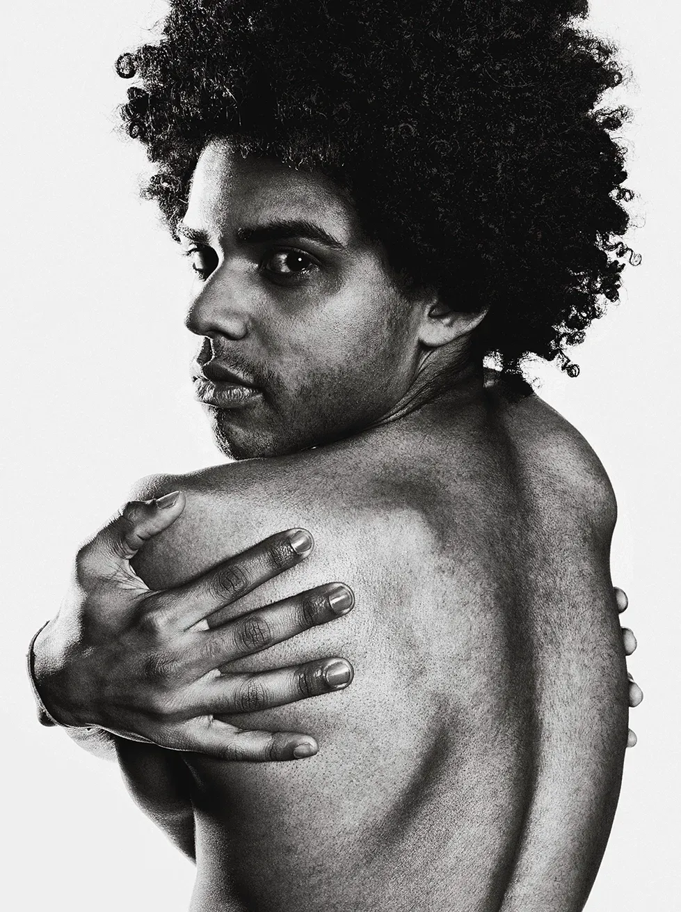Man with afro looks over shoulder, arm across back; black and white.