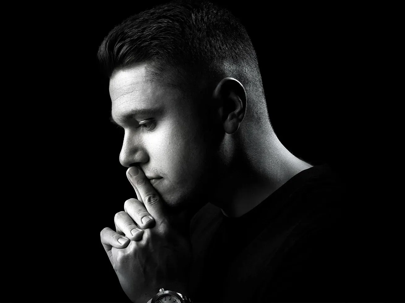 Man in profile, dark setting, hand to chin, thoughtful expression, black and white.