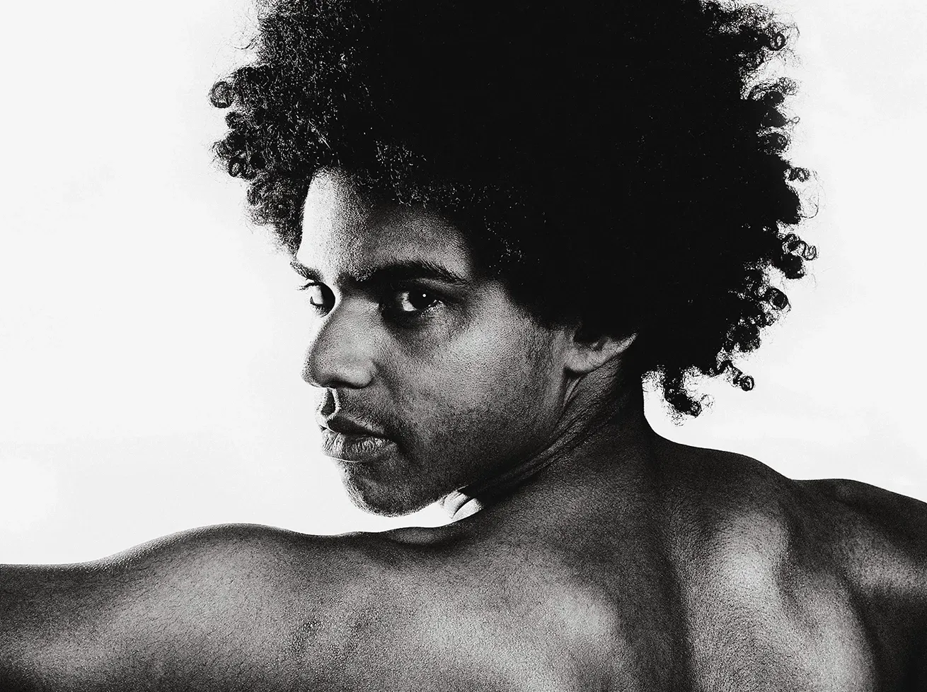 Man with large afro, looking over his shoulder, back partially visible. Black and white studio portrait.