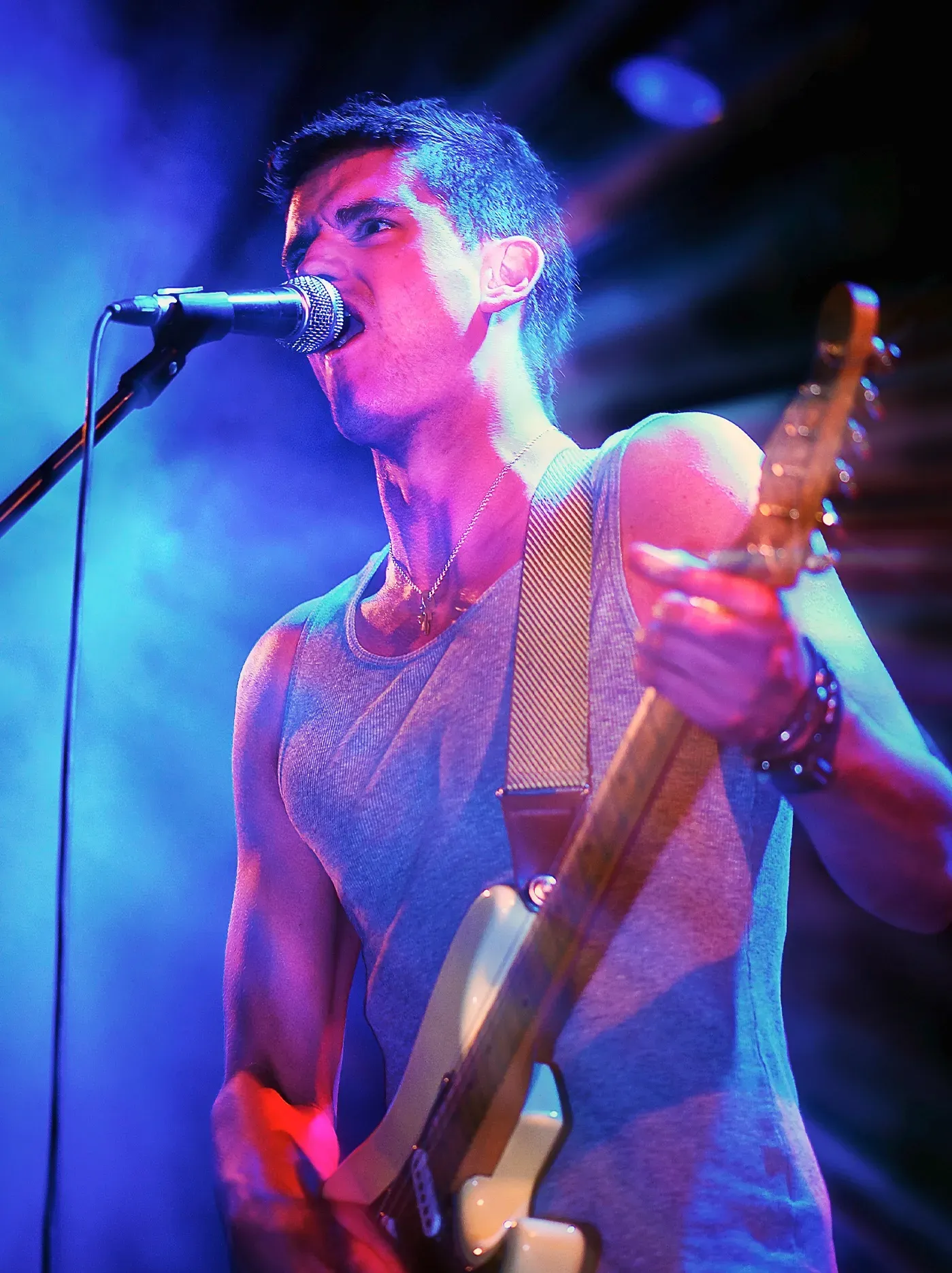 Man singing and playing electric guitar on stage, bathed in blue and pink light.