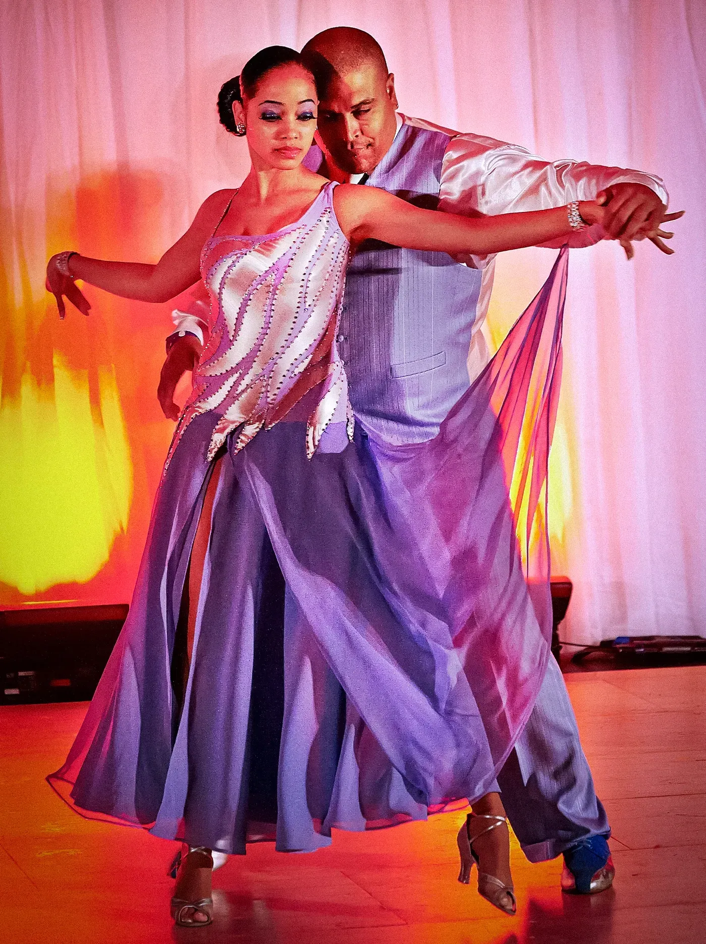 Couple in formal attire dancing, woman in purple gown, man in suit, studio setting.