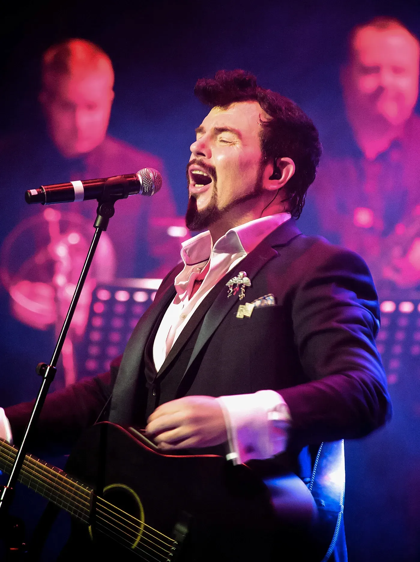 JackL, holding a guitar, and performing on stage with a band.