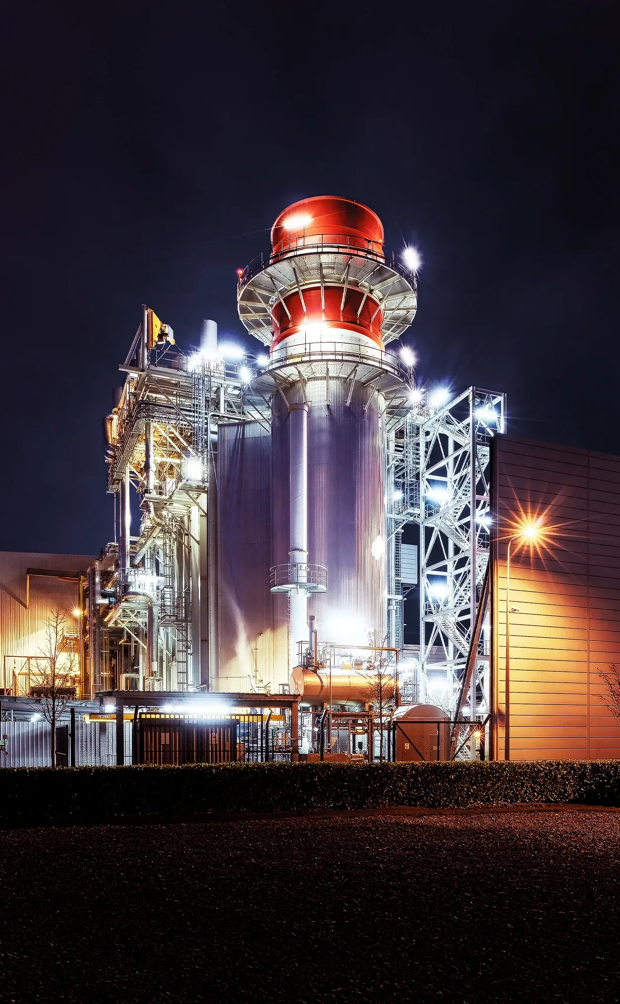 A large industrial power plant at night, illuminated with white and orange lights against a dark sky.