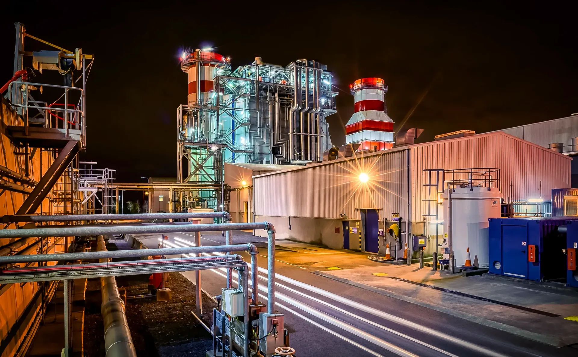 Night view of an industrial power plant with illuminated pipes, towers, and buildings.