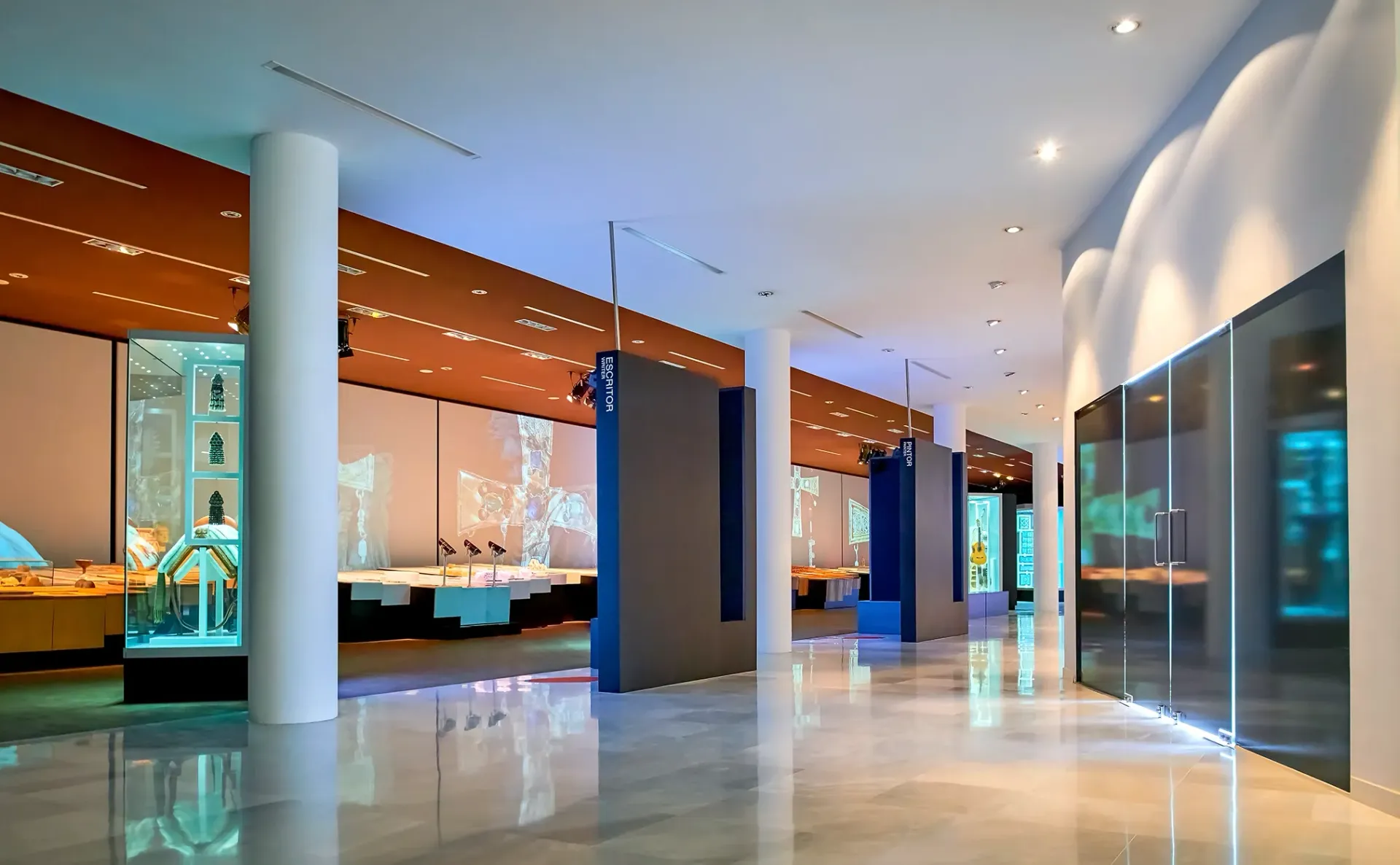 Modern museum hallway with exhibits and glass display cases. Bright lighting, white columns, orange and blue accents.