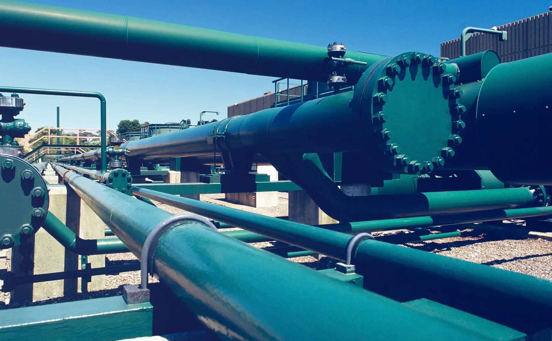 Green industrial pipelines against a blue sky, possibly an oil or gas facility.