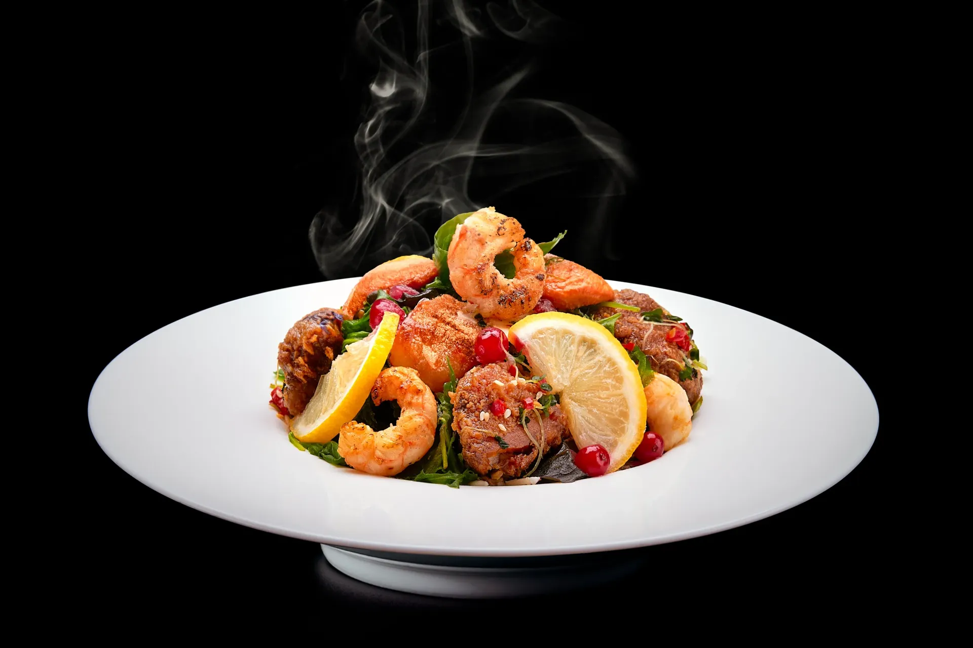 Steaming seafood dish with lemon slices and pomegranate seeds on a white plate against a black backdrop.